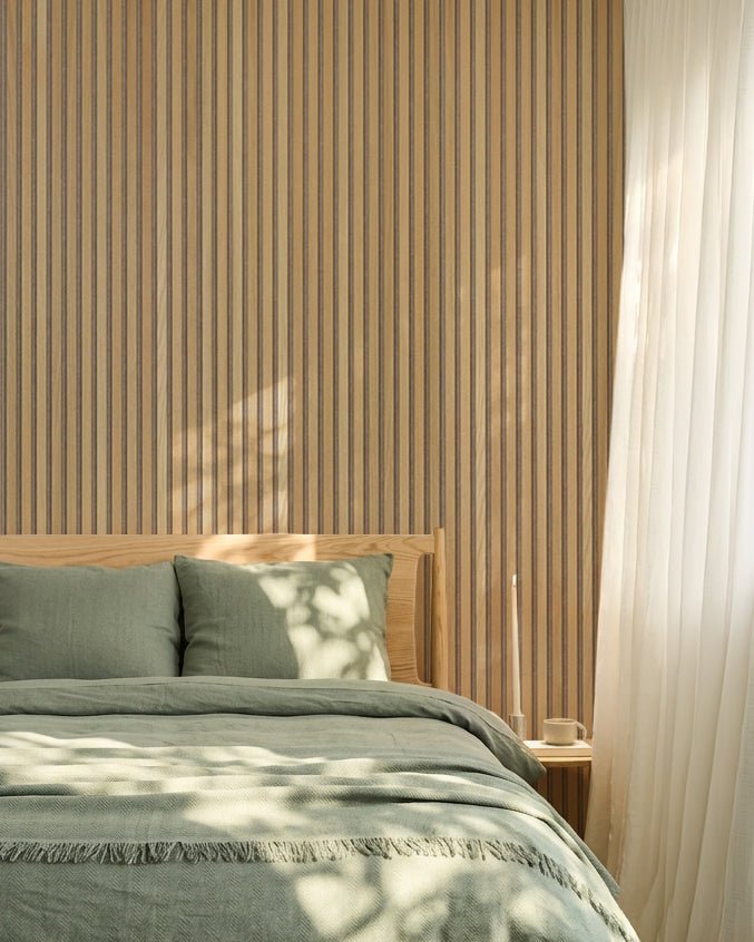Minimalistisk nordisk soveværelse med WoodUpp Akupanel akustikpanelvæg i egetræ, salviegrønt sengetøj, sengeramme i træ og hvide, gennemsigtige gardiner.