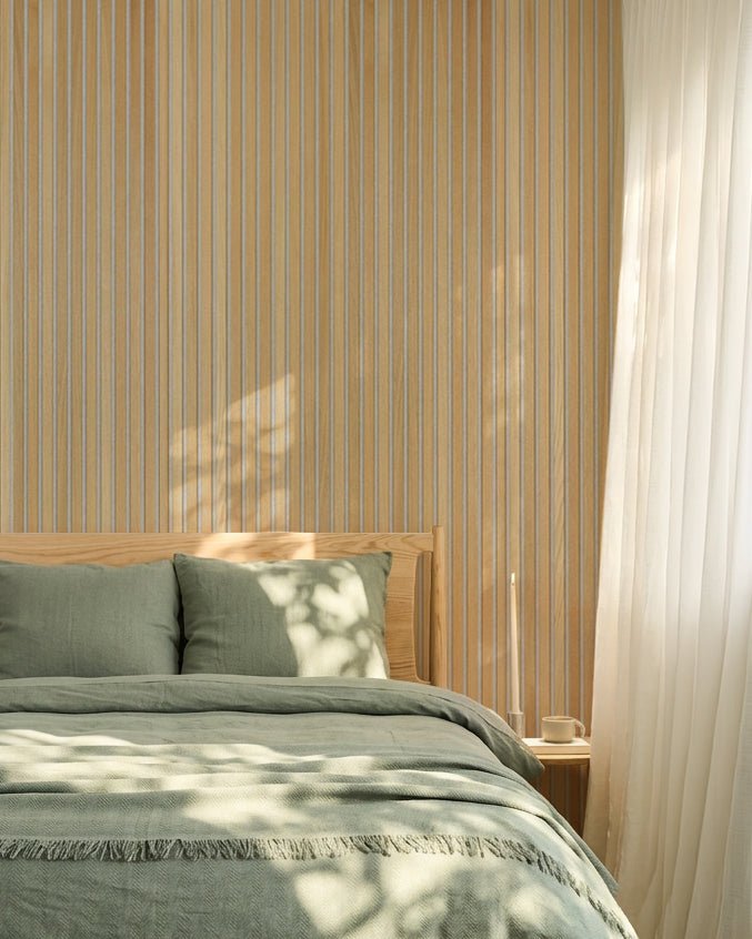 Minimalistisk nordisk soveværelse med salviegrønt sengetøj og en WoodUpp Classic Oak Akupanel akustisk lamelvæg; sollyset skaber bløde skygger på sengen.