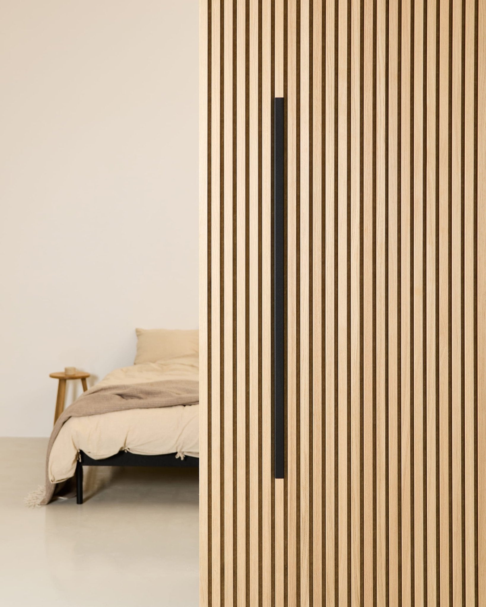 Minimalistisk soveværelse med en beige seng, et sidebord i træ og et WoodUpp Akupanel Black Aluminum 120 cm akustikpanel monteret på væggen.