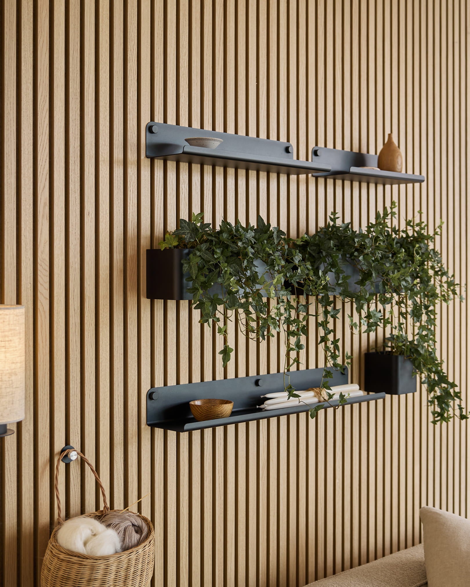Tre sorte Norr | Plant Box-hylder fra WoodUpp med indretning og en plante er monteret over en flettet kurv med garn på en grøn akustisk lamelvæg.
