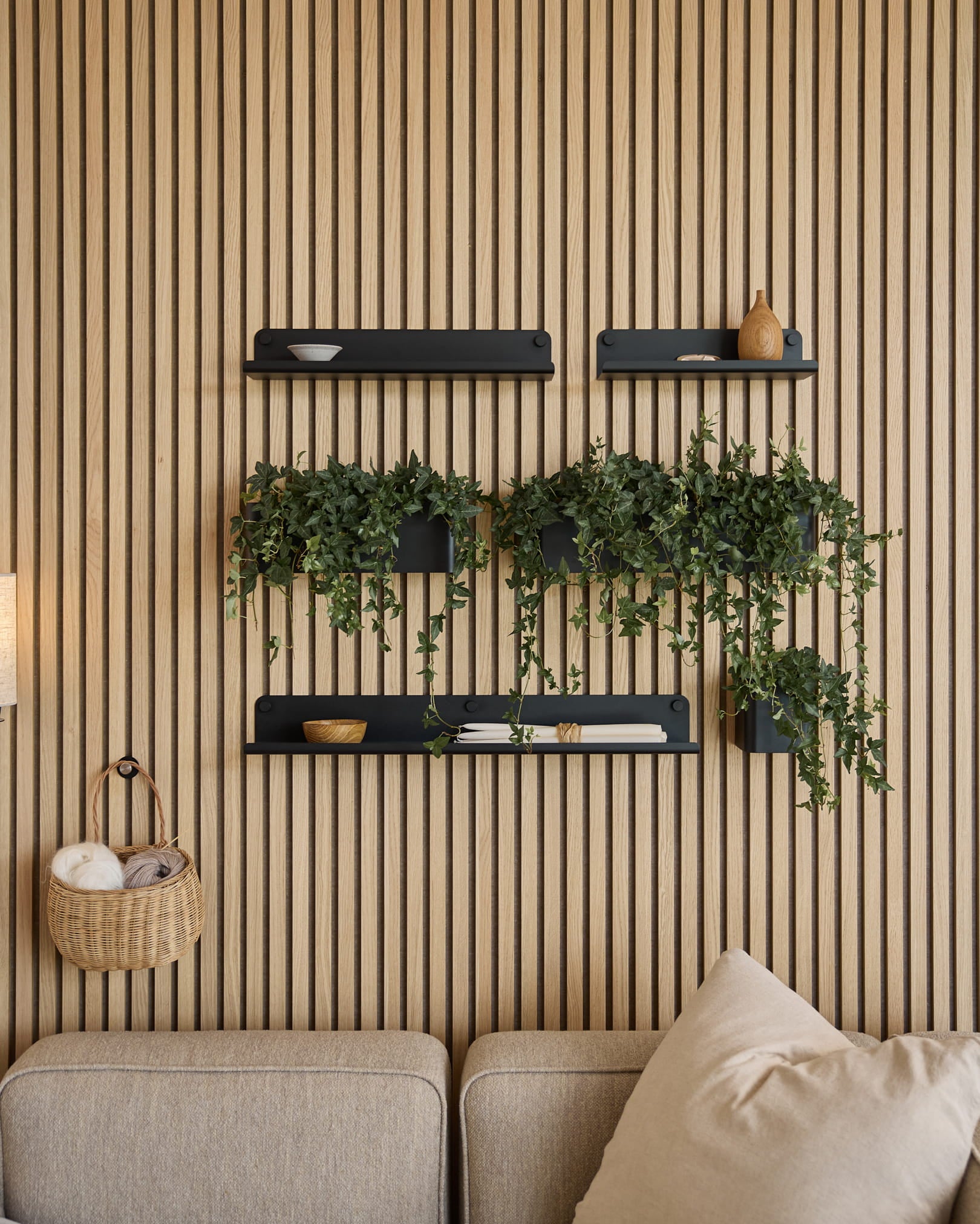 Moderne stue med et nordisk akustisk lamelvægspanel, sorte hylder, slyngplanter i WoodUpps Norr Plant Box (35,9 cm, sort) og en beige sofa.