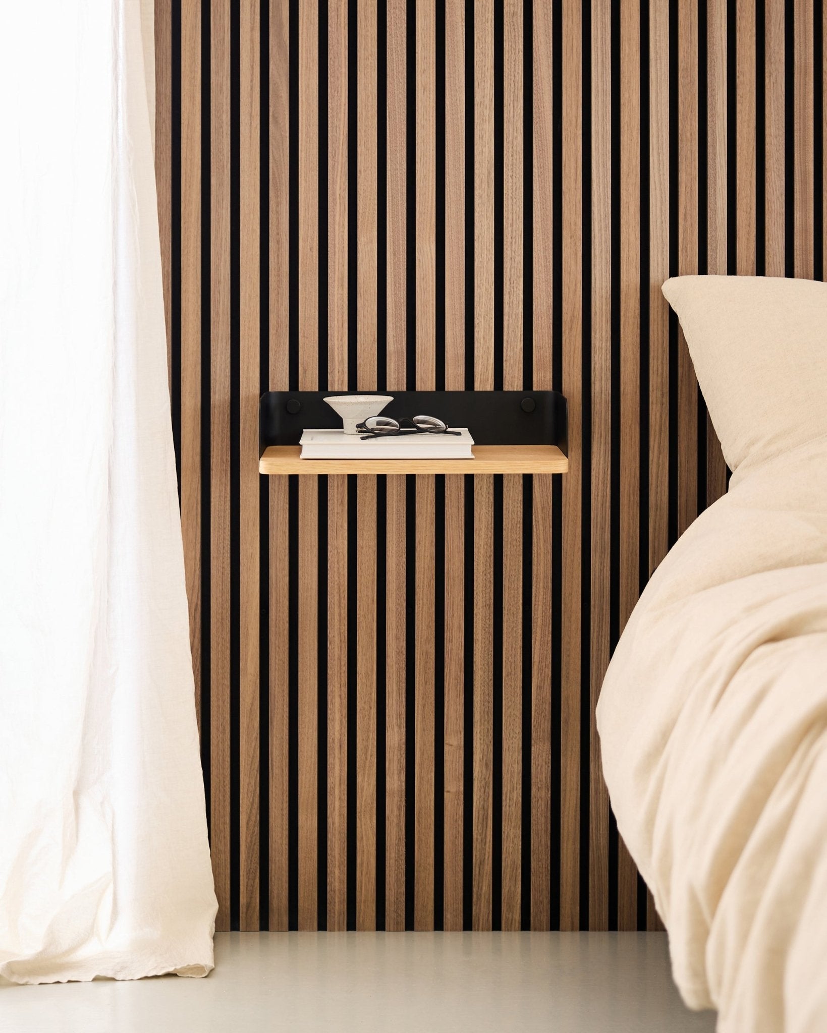 Minimalistisk soveværelse med en nordisk væg med trælameller Akustikpanel, WoodUpp Linn bogreol i Natural Oak og et svævende sengebord ved siden af en beige seng.