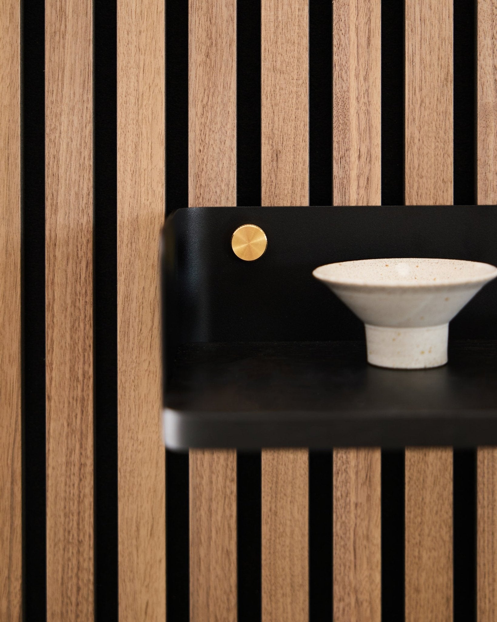 Keramisk skål placeret på Linn Boghylde fra WoodUpp, 39,9 cm i black oak med vertical black lameller og en brass accent, som afspejler nordisk minimalistisk design.