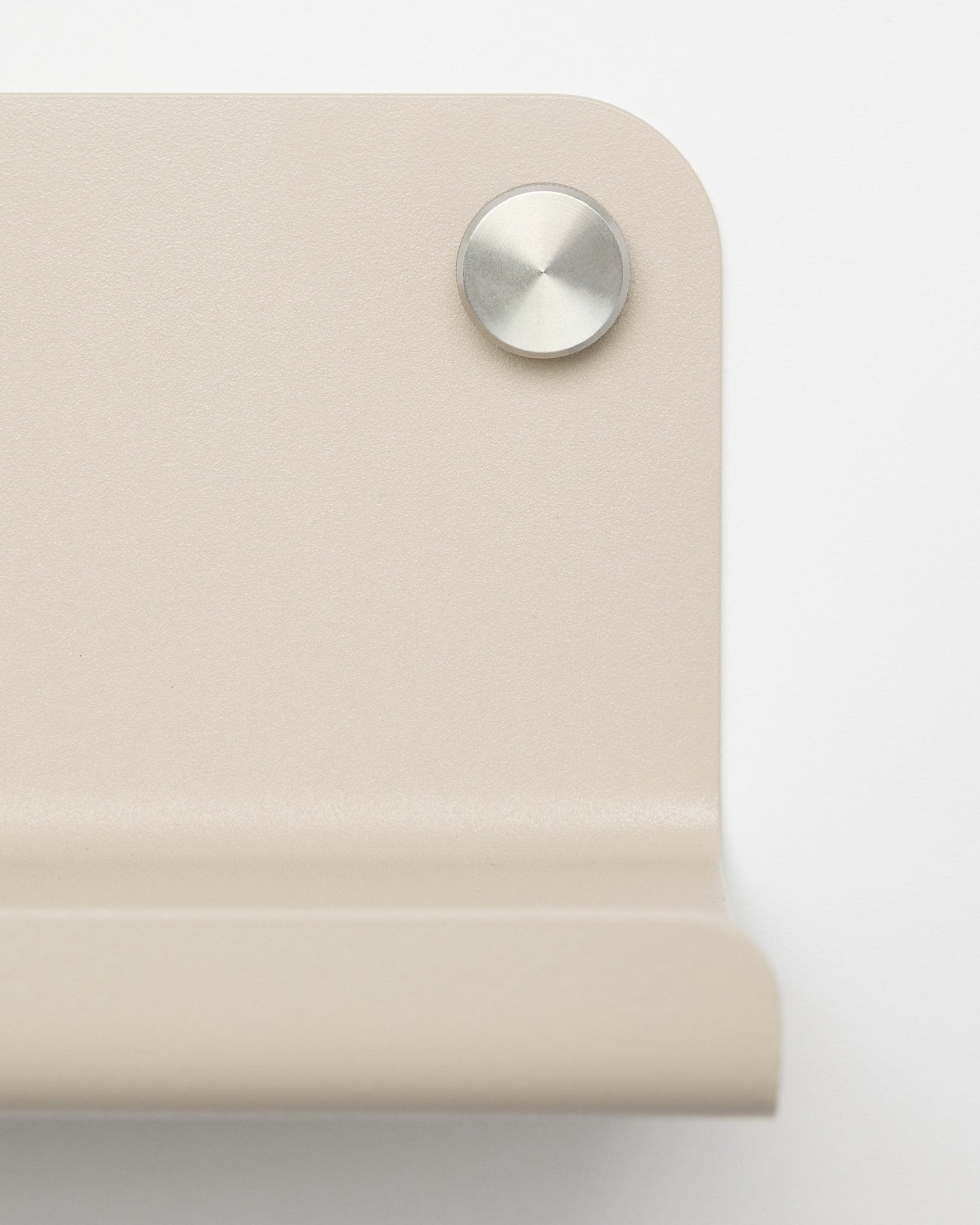 Nærbillede af et beige metalhjørnebeslag med en rund sølvskrue, designet til WoodUpp Norr bred hylde, 35,9 cm, vist mod en hvid baggrund.