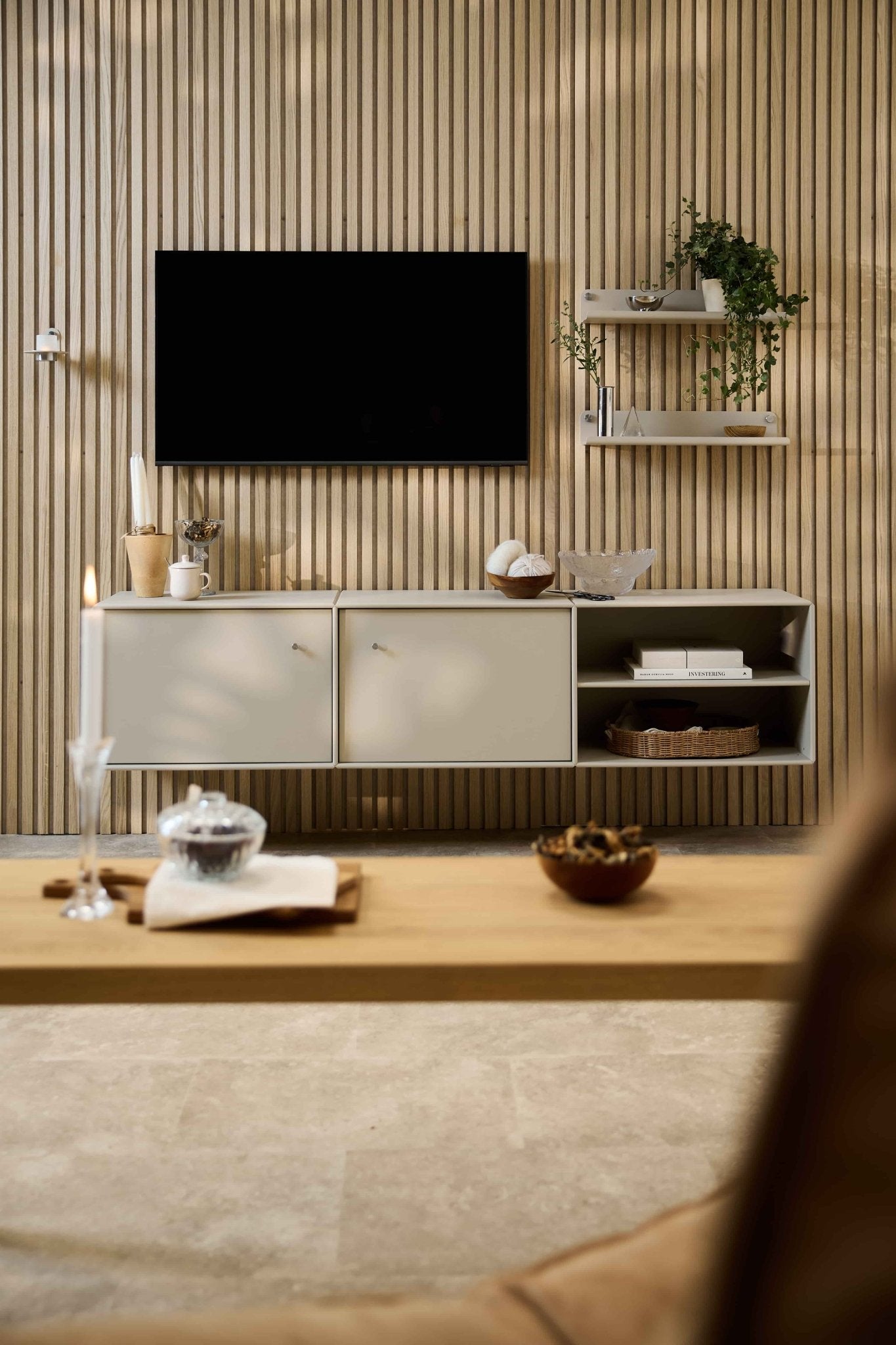 Moderne stue med Arka TV-bord fra WoodUpp, modulopbyggede siddepladser, nordiske hylder med planter og dekorationer samt et stearinlys på sofabordet.