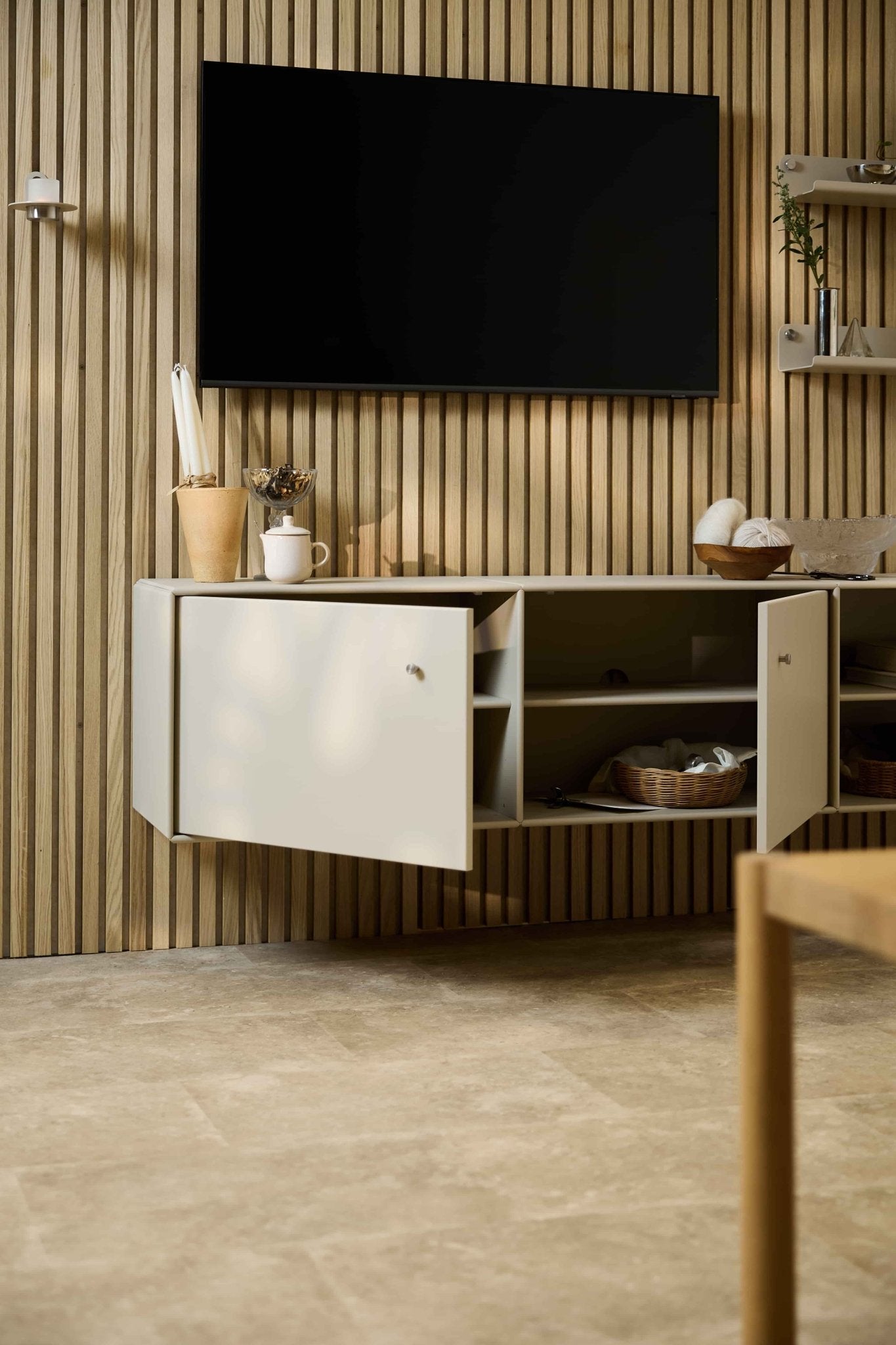Moderne stue med Arka-tv-bænken i beige fra WoodUpp placeret under et skab og et tv på en nordisk Akupanel-væg med akustiske trælameller. Modulmøbler.