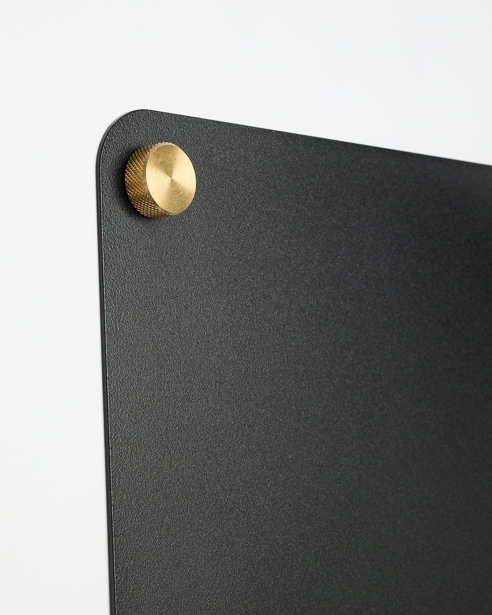 Close-up of a large black Norr Magnetic Board by WoodUpp, part of the CREATE collection, featuring a round gold-colored metal fastener in the top corner.