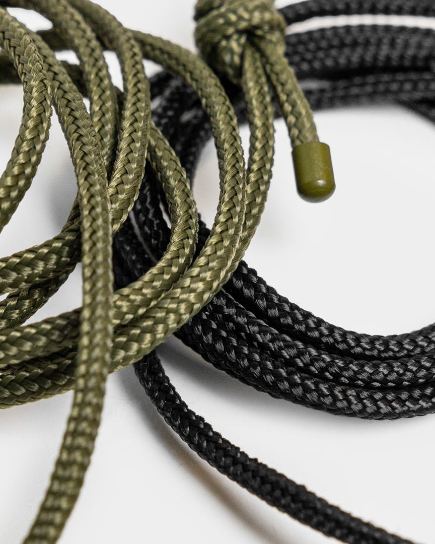Vindar | Gallery String fra WoodUpp: flettet grøn og black snor med plastspidser, vist ved siden af en fotosnor på en hvid baggrund.
