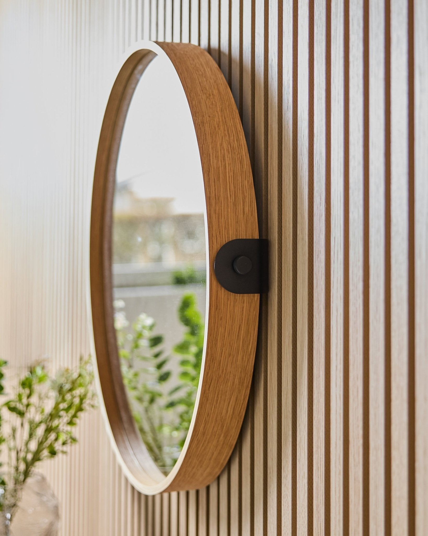 Linn | Mirror / Natural Oak fra WoodUpp monteret på en stribet væg med Akustikpanel, der reflekterer grønne planter og naturligt lys fra et nærliggende vindue.
