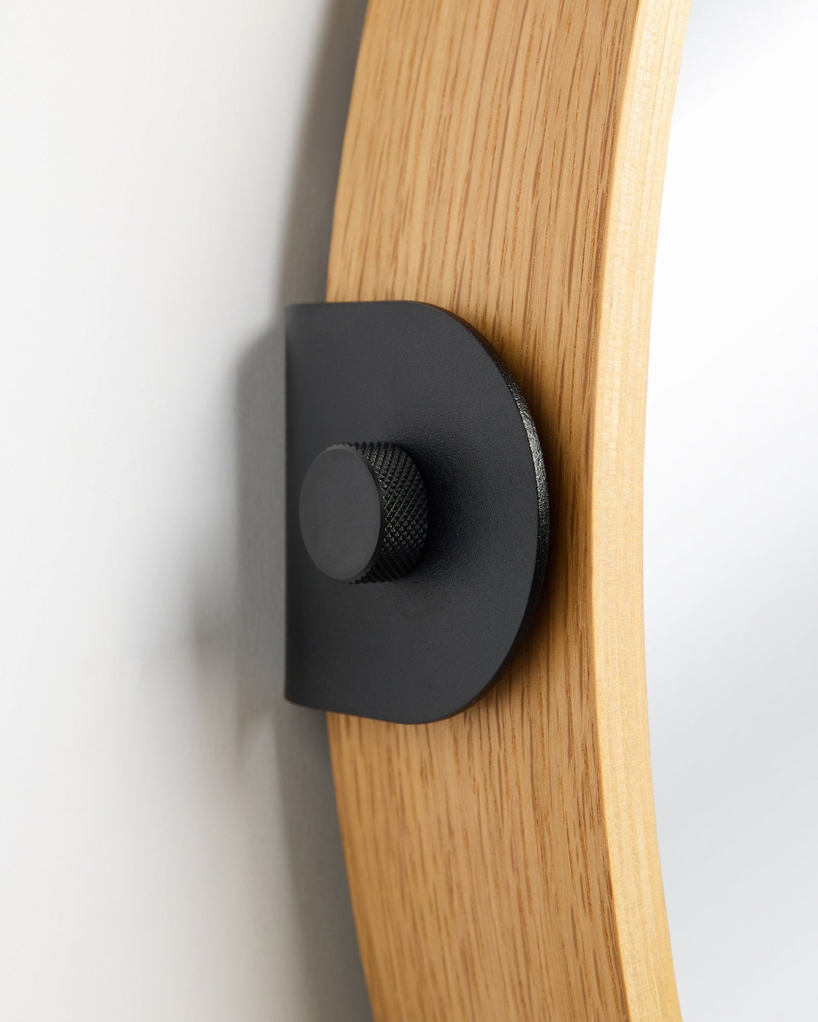 Detalje af WoodUpp Linn Mirror i Natural Oak, et Akustikpanel monteret på væggen med et metalbeslag i black og en rund knop.