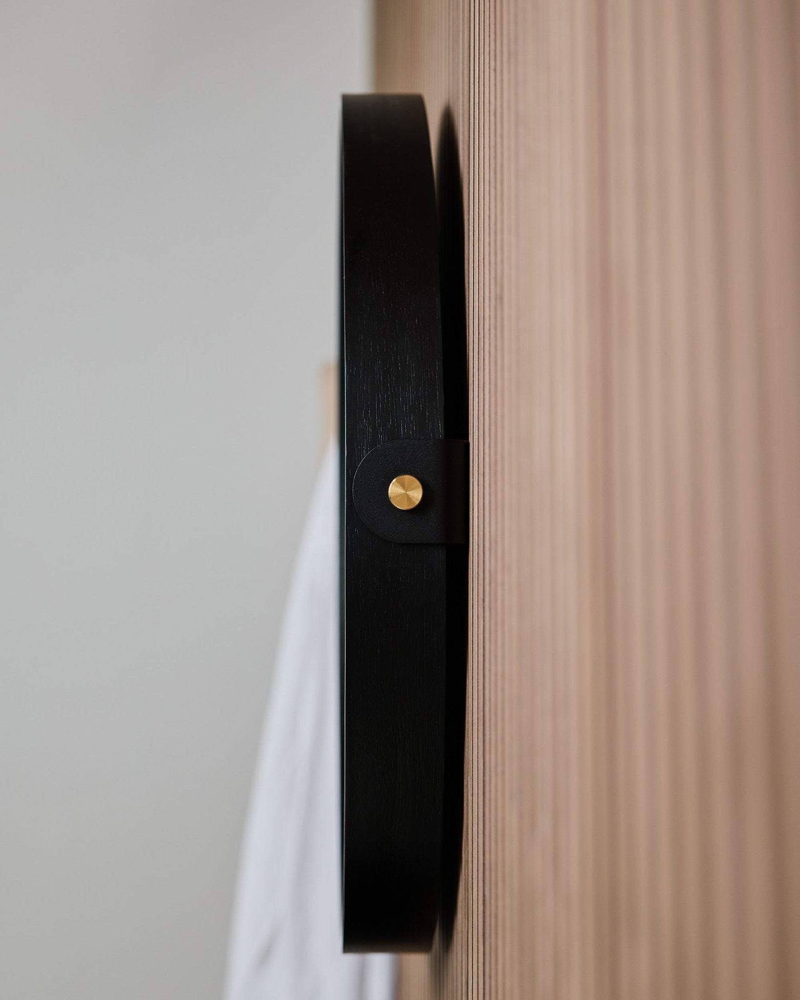 Nærbillede fra siden af WoodUpp Linn | Mirror / Black Oak vægkrog, monteret på et rillet egetræs-Akustikpanel, designet til at hænge et rundt spejl på.
