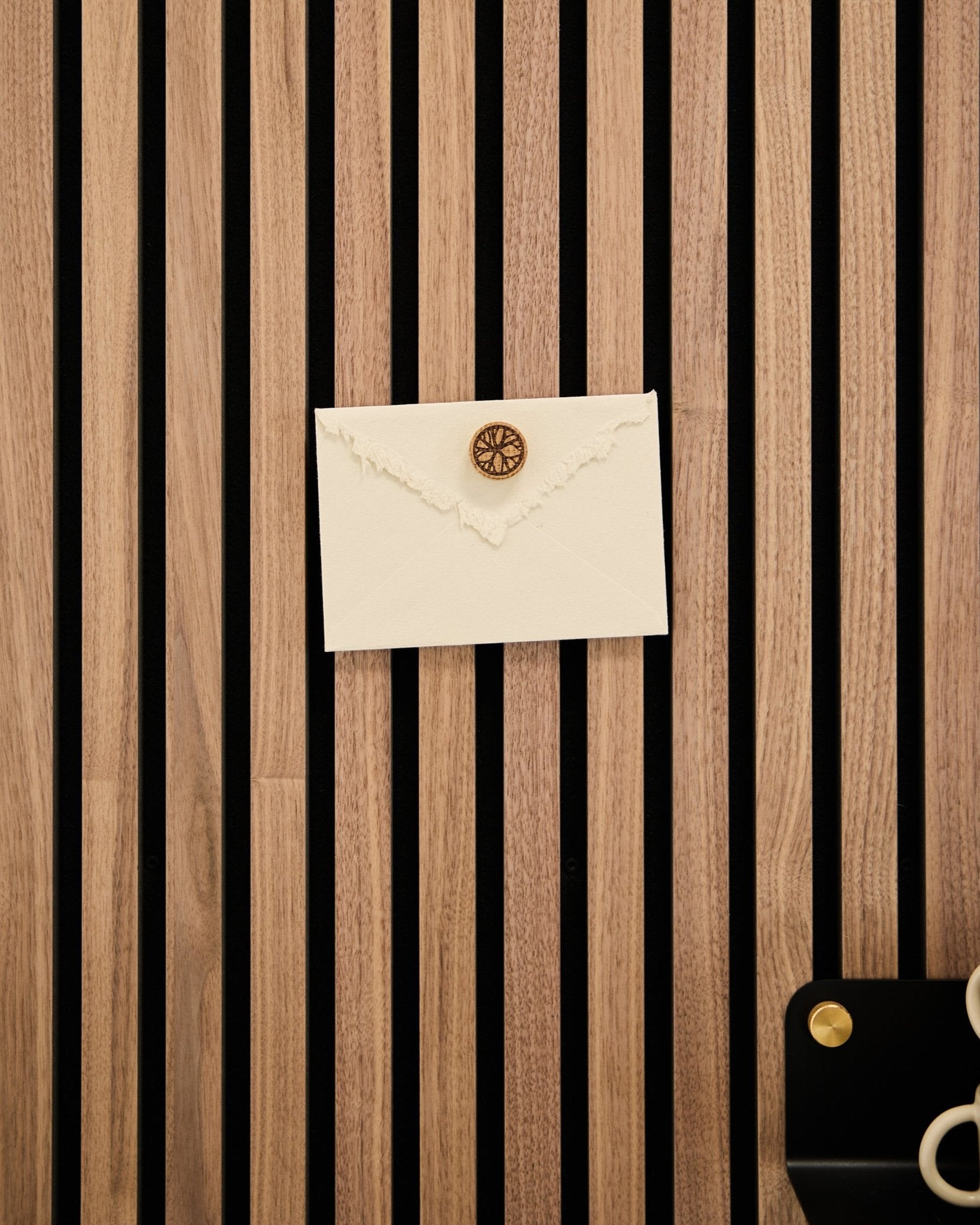 En cremefarvet kuvert med vokssegl er fastgjort til et WoodUpp akustisk lamelvægspanel i egetræ med Norr Poster Magnet-sættet i Natural Oak; en saks og en bakke står i nærheden.