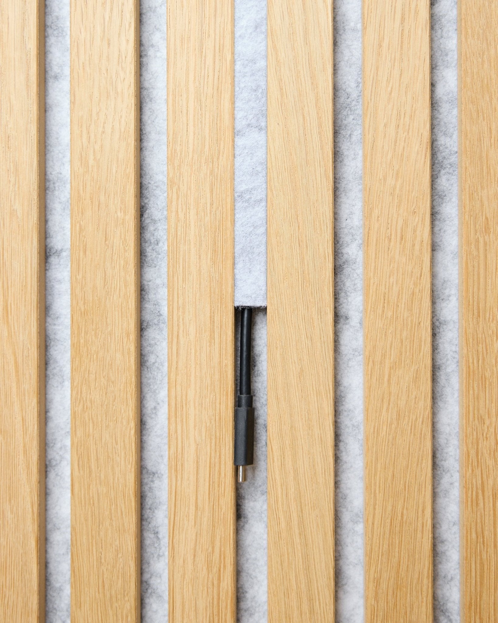 Dupps Pop-on Cable Cover-sæt (grey, 3 stk.) fra WoodUpp holder styr på kabler mellem lyse Akupanel akustiklameller i træ på en hvid, tekstureret baggrund.