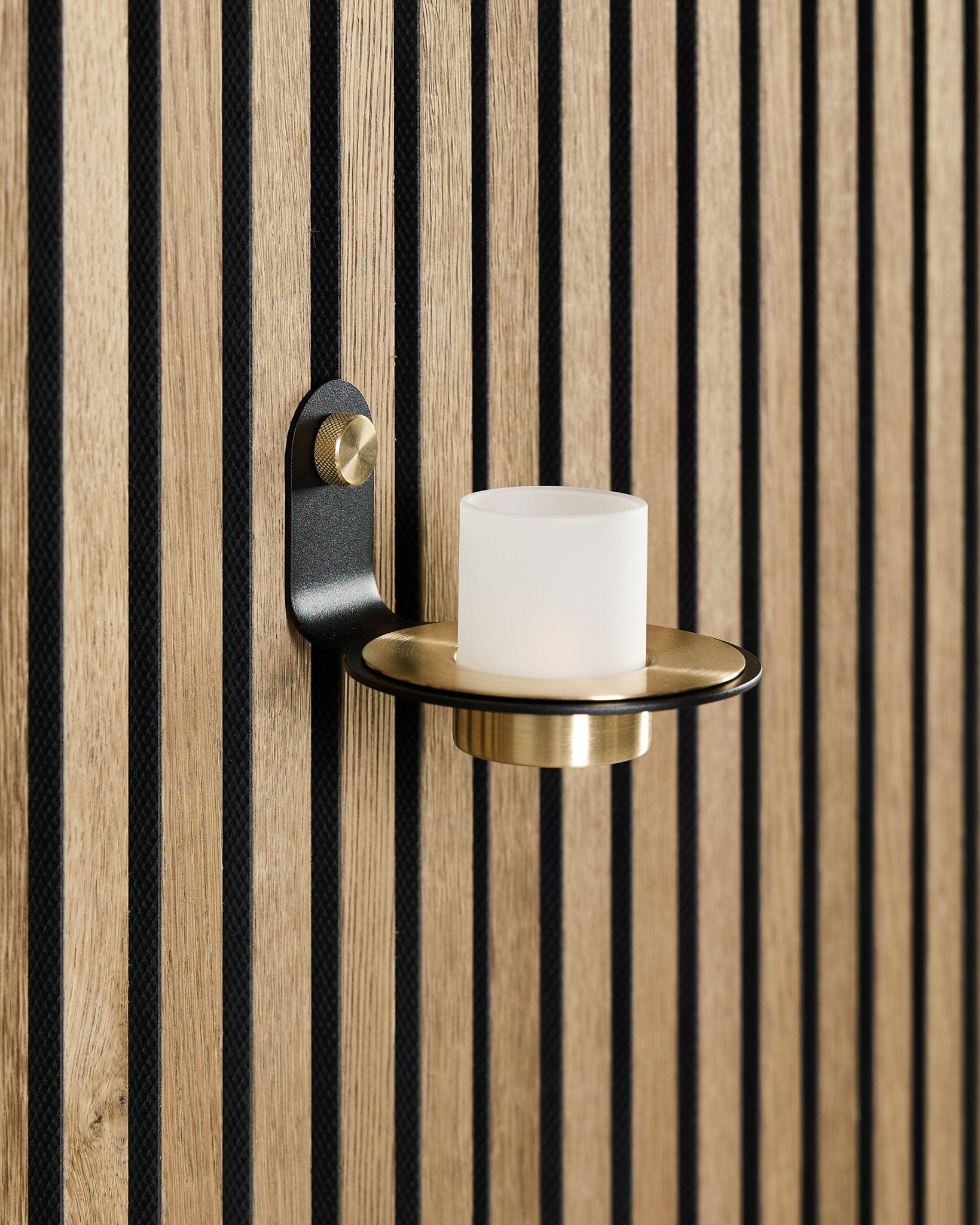 Norr lysestage i black og brass fra WoodUpp er monteret på et nordisk Akupanel akustiktræpanel med vertical black lameller.