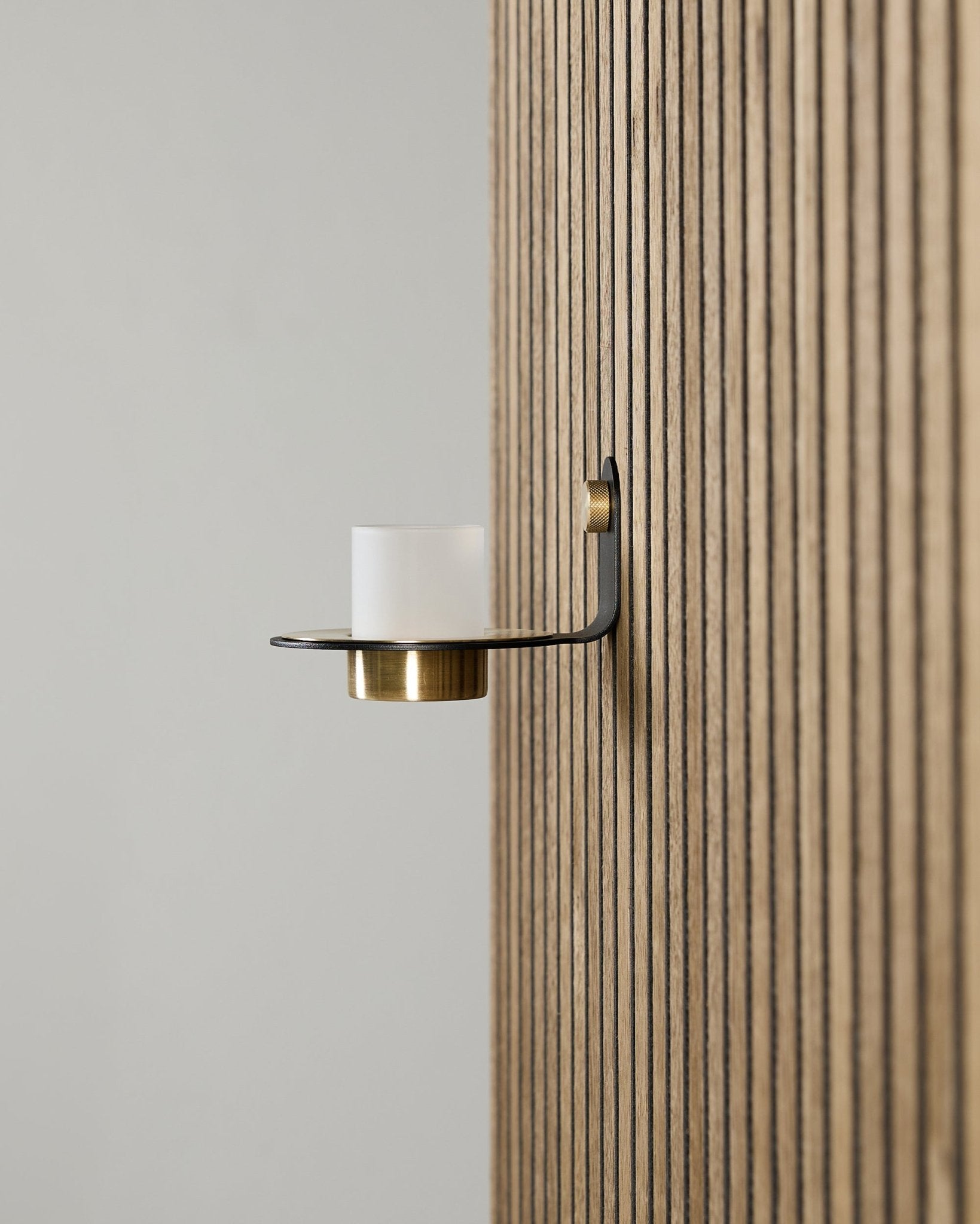 Norr Candle Holder i black og brass fra WoodUpp monteret på et vertical Akupanel Akustikpanel, med matteret glas og detaljer i brass.