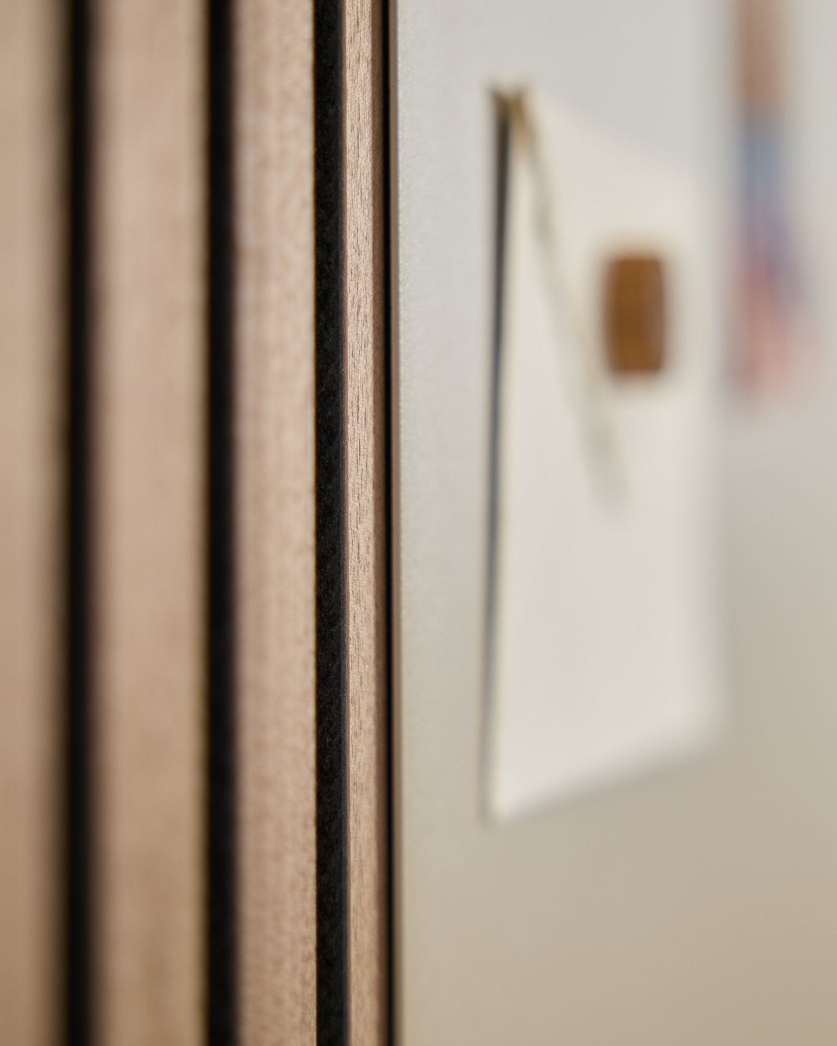 Nærbillede af et WoodUpp Akupanel akustik træpanel med vertical lameller, ved siden af en sløret large beige Norr magnettavle i baggrunden.
