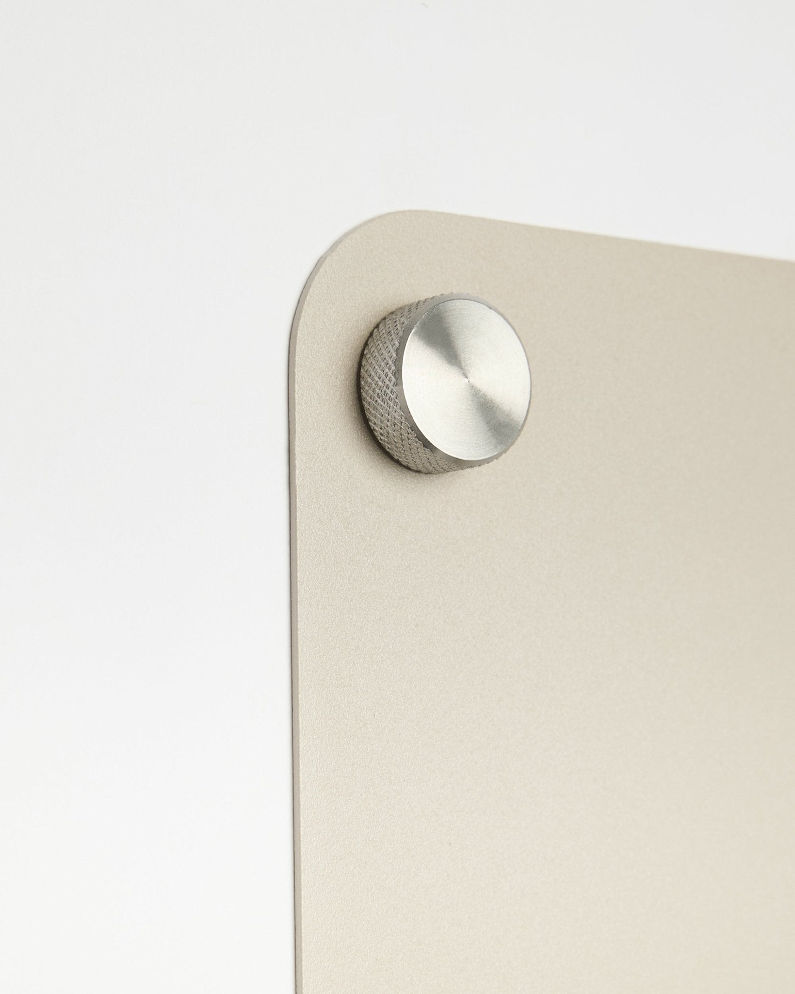 Nærbillede af et rundt knoptilbehør i metal, fastgjort til den large beige Norr magnettavle fra WoodUpp, med en detalje i frostet glas på en hvid baggrund.