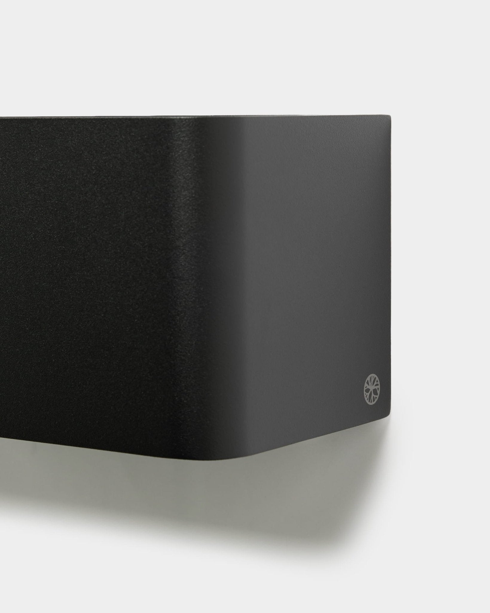 Nærbillede af den minimalistiske WoodUpp Norr Plant Box (23,9 cm, sort) med afrundede kanter og logo, monteret på en hvid væg. Nordisk design af akustisk tilbehør.