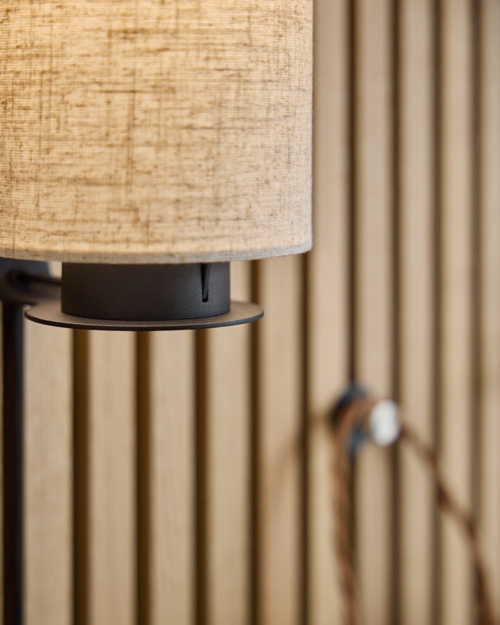 Feya Wall Lamp / Black/Beige af WoodUpp med en beige skærm af hørbomuld, sort metalbase og synlig ledning monteret på et nordisk akustisk lamelvægspanel.