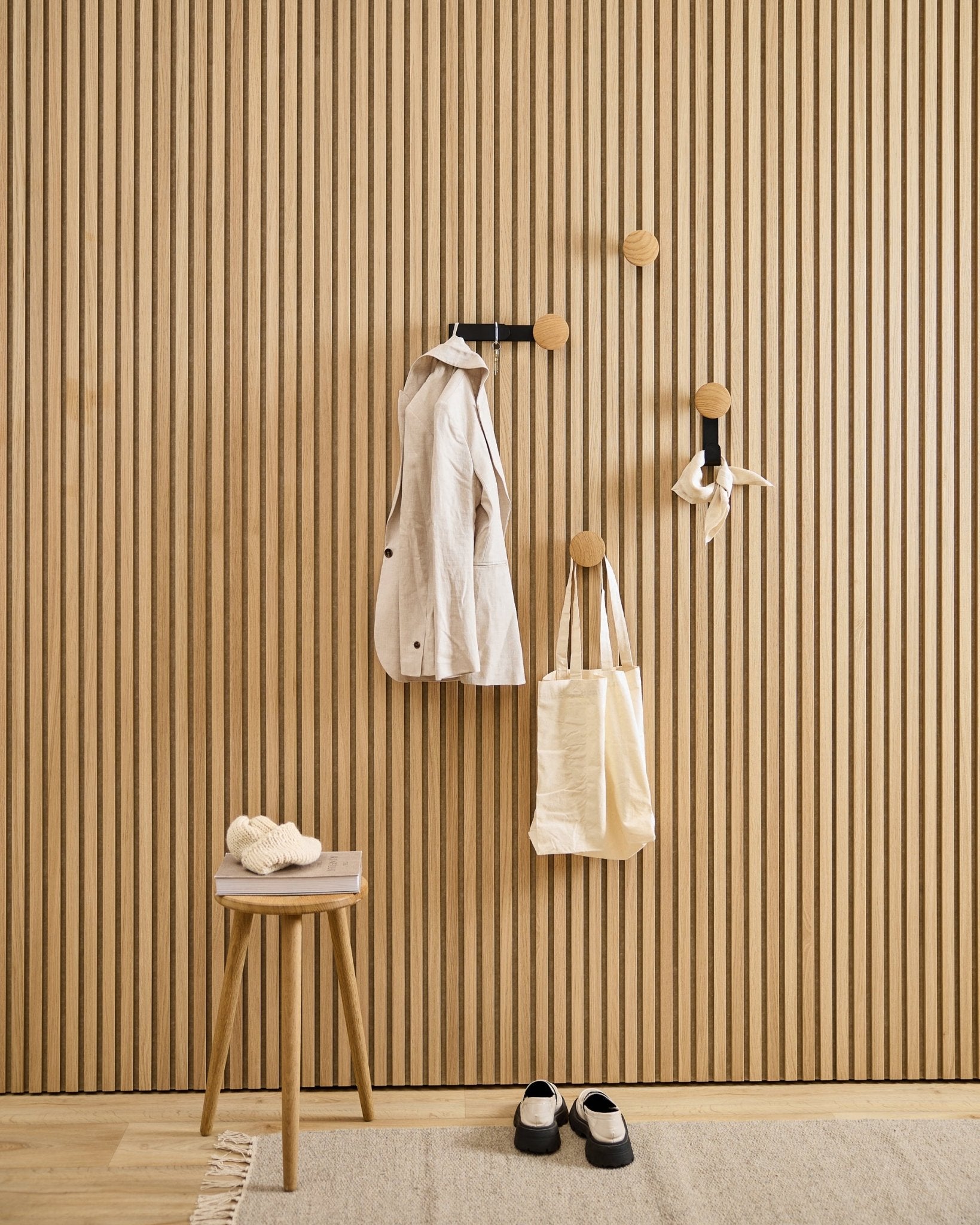 Minimalistisk entré med WoodUpp Linn Vertical knage i natural oak, med en beige frakke, mulepose, halstørklæde, skammel med hjemmesko og black-og-hvide sko.
