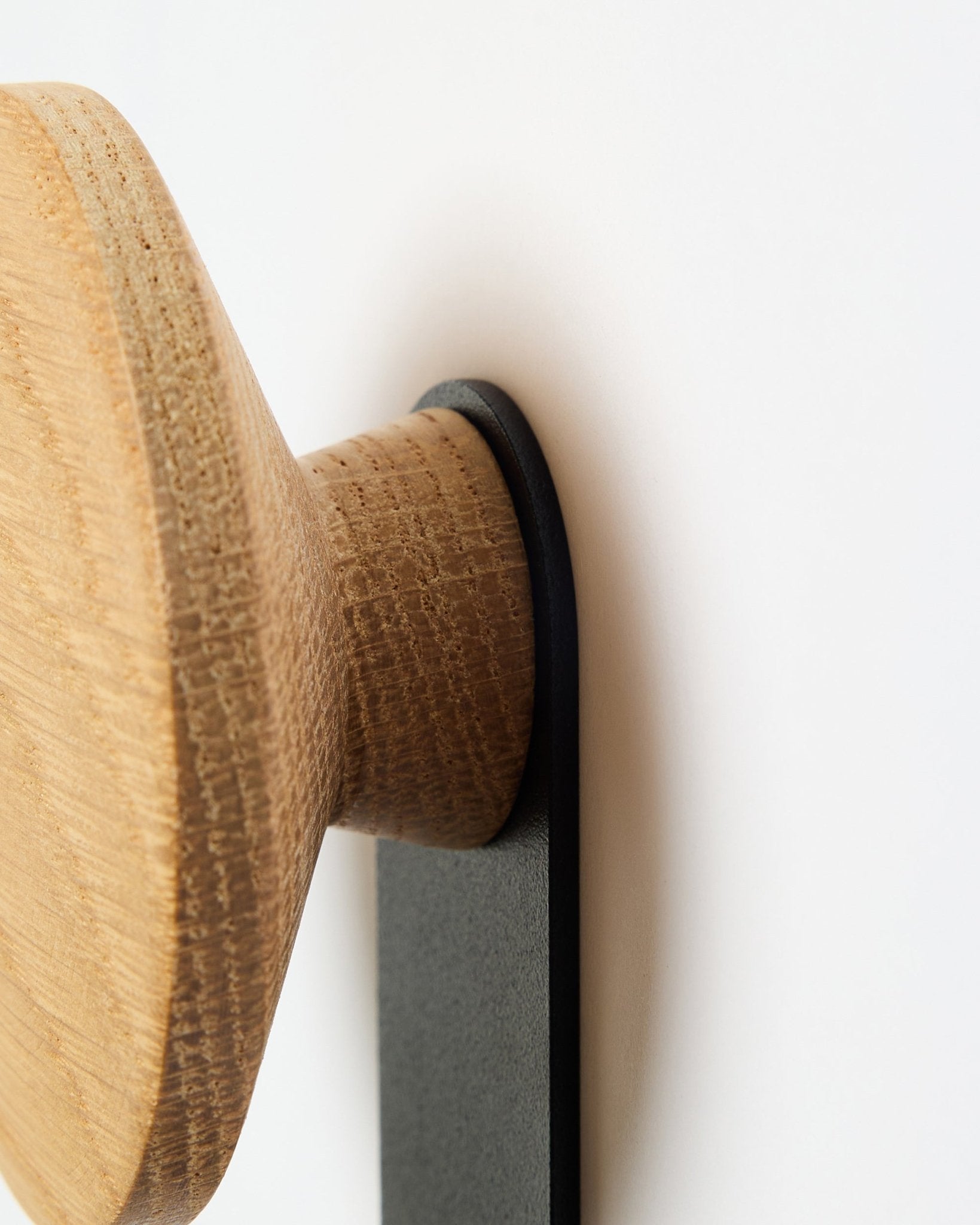 Nærbillede af Linn Vertical knagen i natural oak fra WoodUpp, et rundt trægreb monteret på et black beslag, designet til Akupanel akustikpaneler.