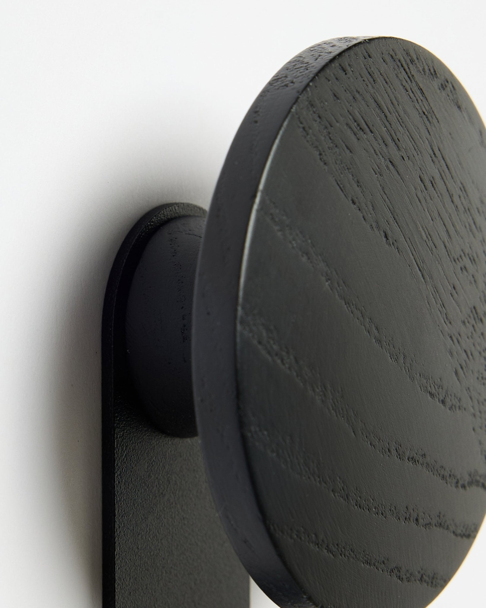 Nærbillede af WoodUpp Linn | Vertical Hanger i Black Oak, der fremhæver de fine årer i træet mod en hvid Akupanel Akustikpanel baggrund.