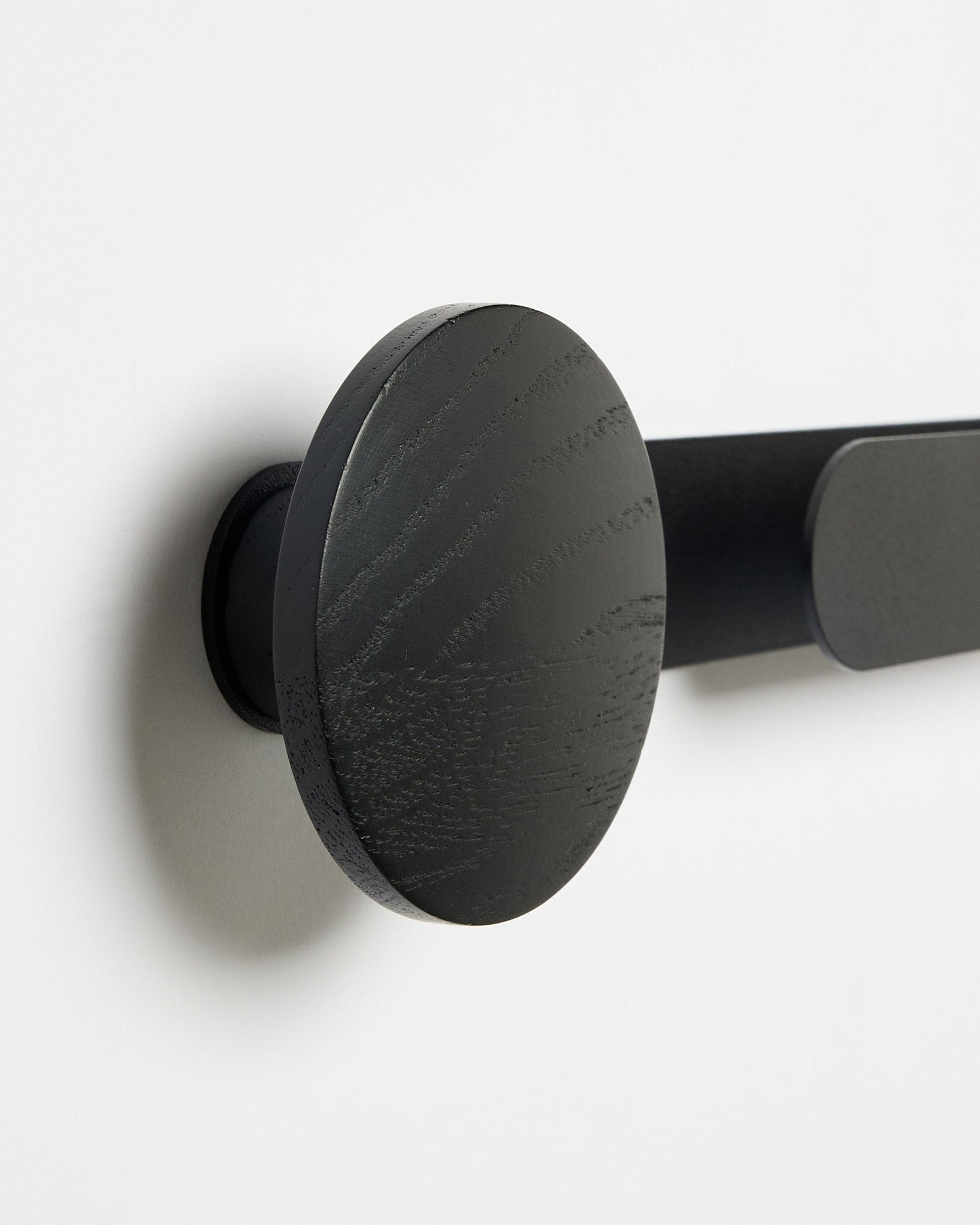 Nærbillede af WoodUpp Linn | Horizontal Hanger i Black Oak med mat black finish, monteret på en hvid væg; tilbehør til akustikpaneler i træ.