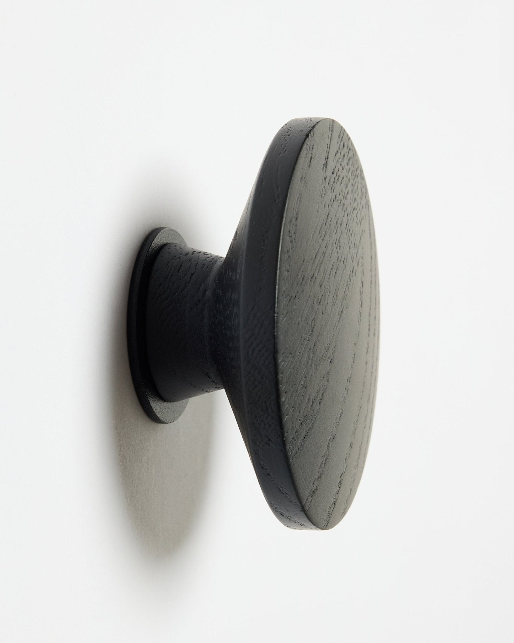 En rund Linn | Single Hanger fra WoodUpp i black oak, designet som tilbehør til Akupanel akustiske træpaneler, monteret på en hvid overflade med en blød skygge mod venstre.