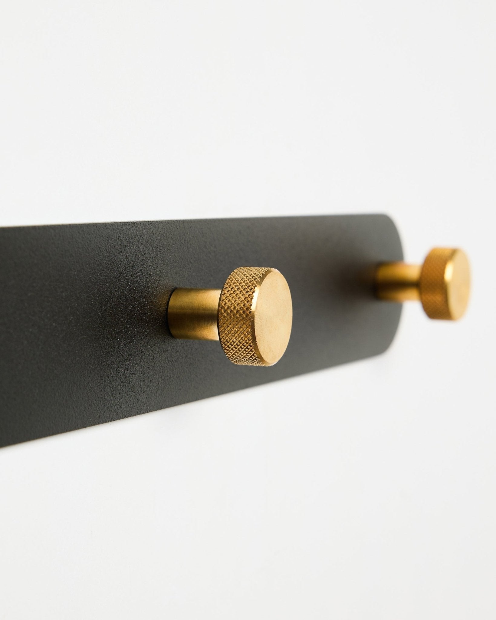 WoodUpp Norr knagerække, model X7, med to cylindriske black og brass kroge på et black beslag, vist mod en hvid baggrund.