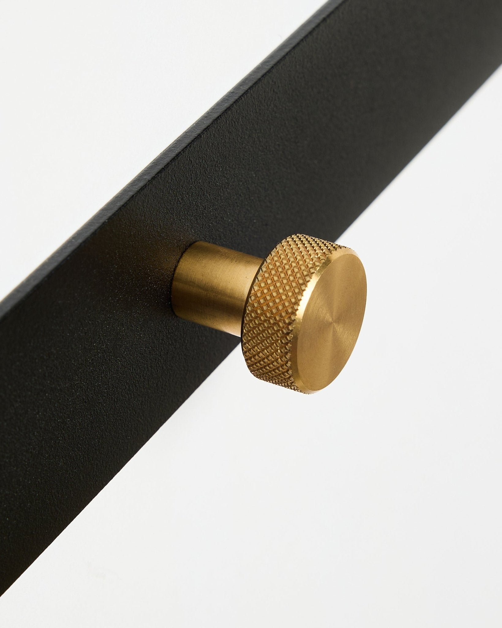Nærbillede af Norr Coat Hook Rack X5 fra WoodUpp med black pulverlakeret steel og runde, teksturerede brass knopper, vist mod en hvid baggrund.