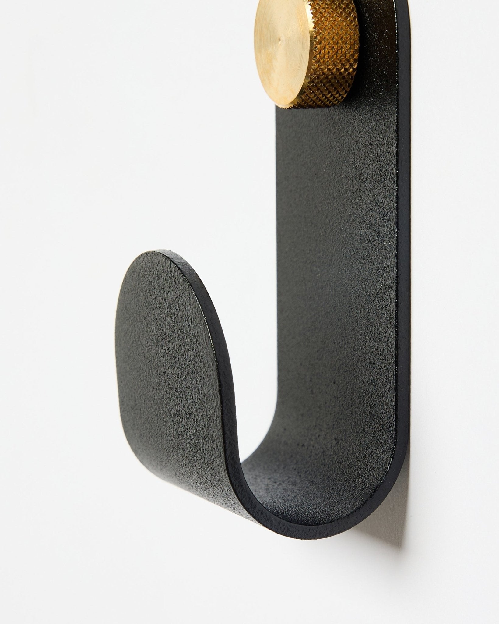 Norr Single Hanger fra WoodUpp har en buet metalarm i black med en guldfarvet afslutning og er designet som et tilbehør til brug med akustikpaneler på hvide vægge.