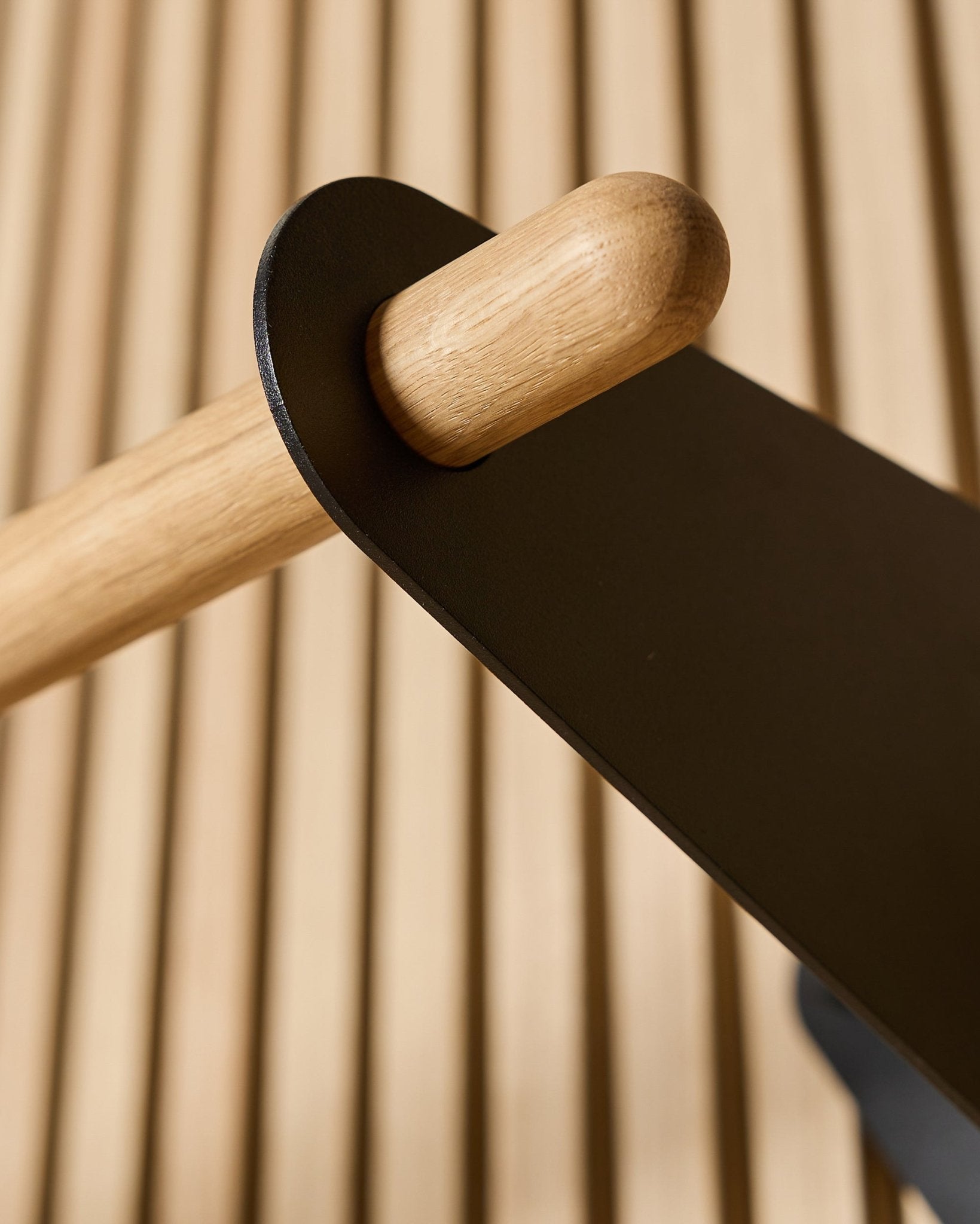 Nærbillede af WoodUpp Linn Coat Rail i black, 75,9 cm, med en stang i massiv eg monteret i et black metalbeslag på et Nordic akustisk lamelpanel.