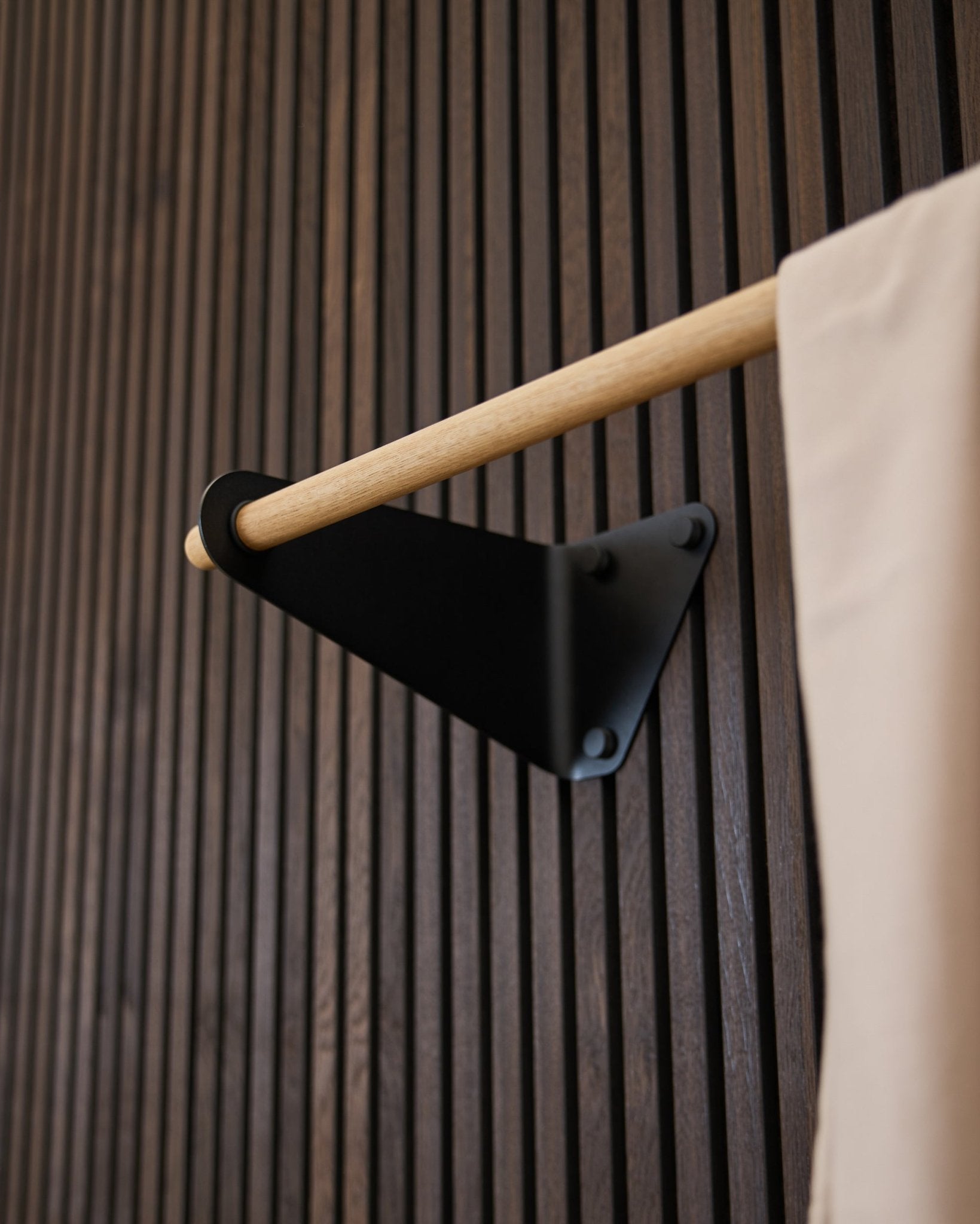 Linn knagerække fra WoodUpp i black (115,9 cm) monteret på et mørkt rillet Akupanel Akustikpanel med beige stofdetalje og black beslag.