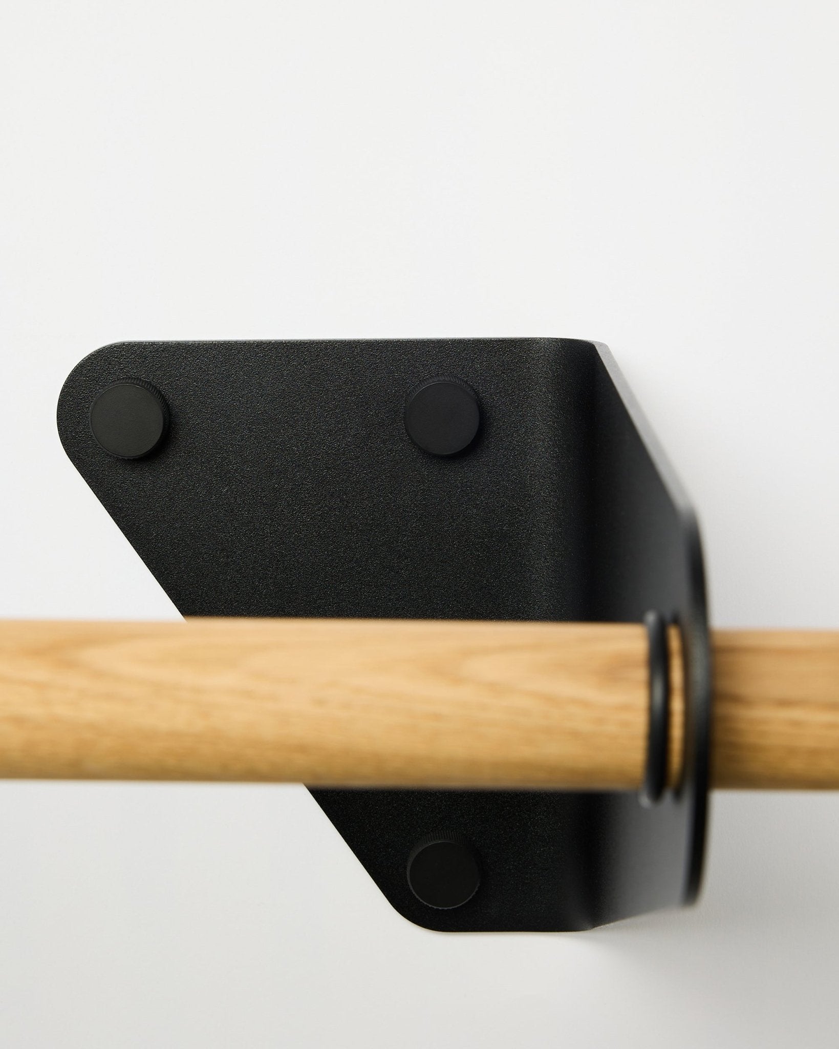Nærbillede af WoodUpp Linn knagerække i black, 115,9 cm, monteret på en hvid væg med et trekantet metalbeslag, vist som en del af nordiske akustiske accessories.