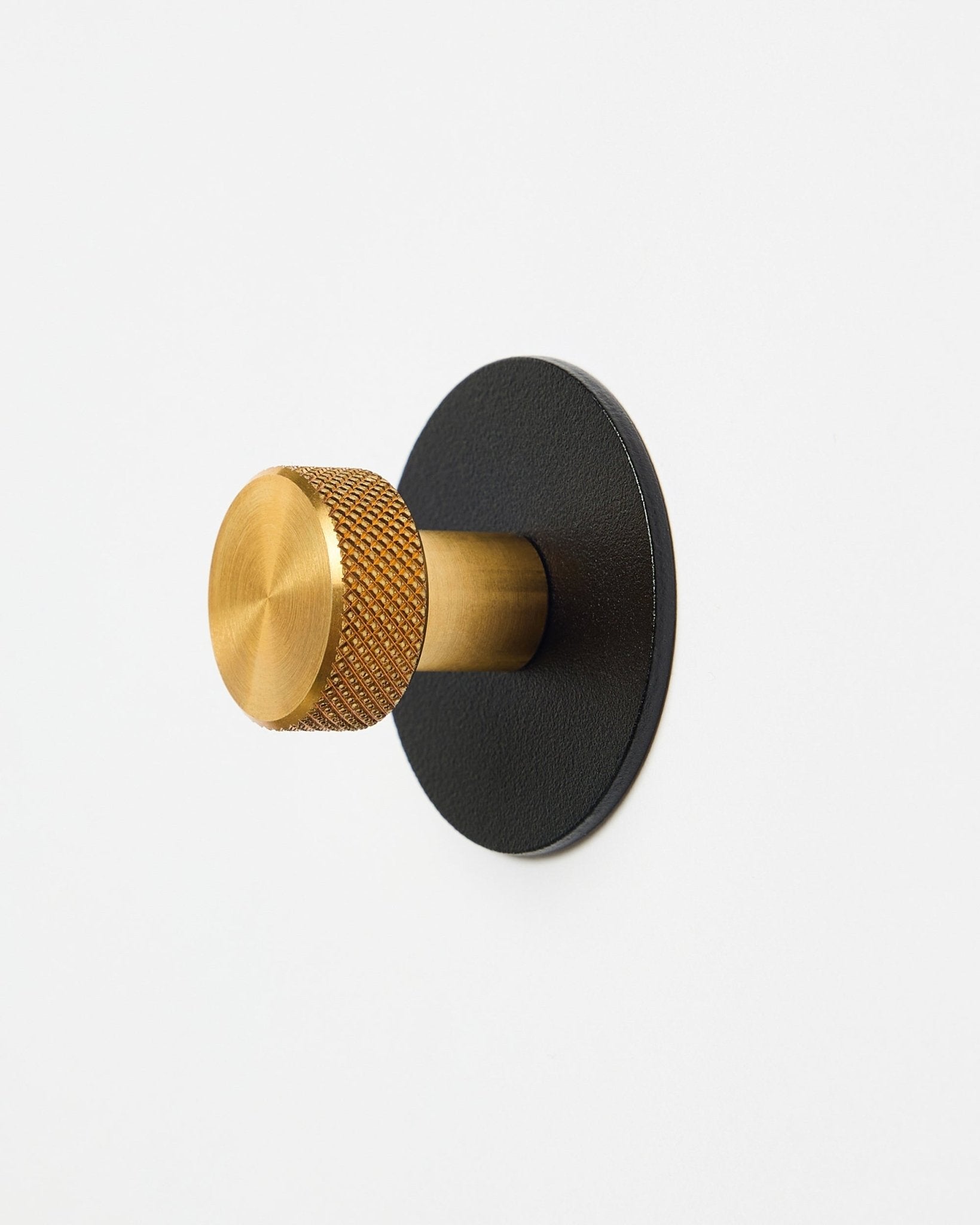 Norr Coat Hook X1 fra WoodUpp med en tekstureret brass knop og black pulverlakeret steel base, tilbehør til Akupanel, vist på hvid baggrund.