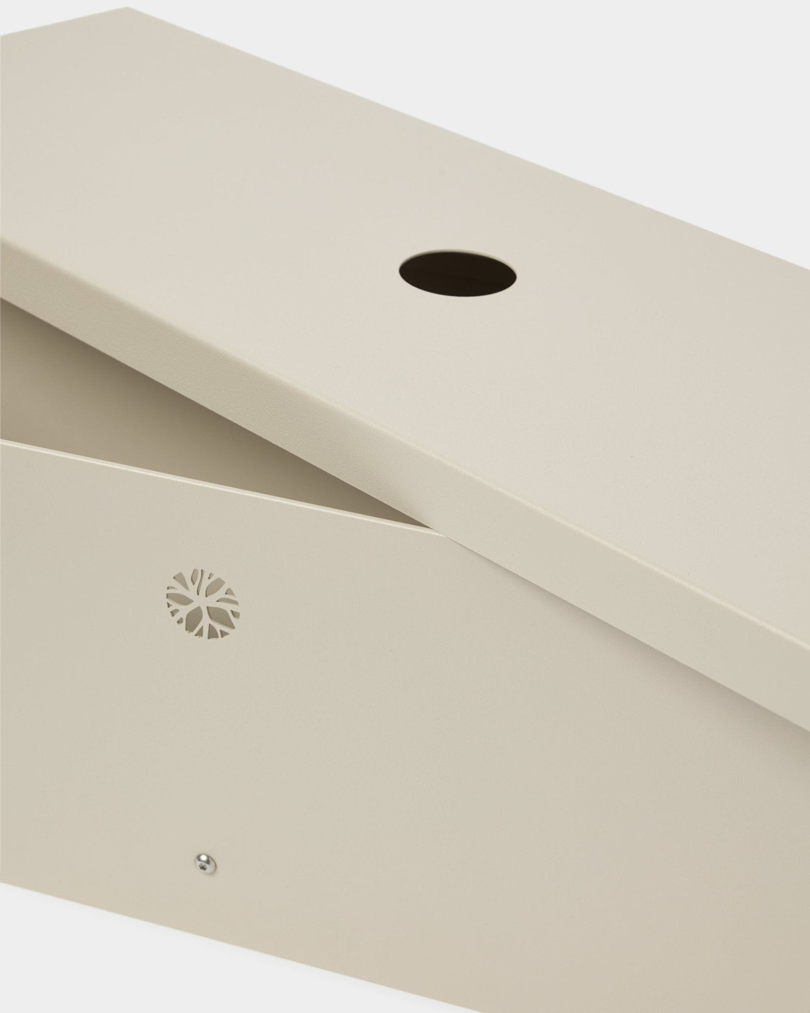 Nell | Metal Box / BM2, Beige fra WoodUpp er fremstillet i pulverlakeret steel med et skråt låg, rund åbning og et diskret emblem på siden.