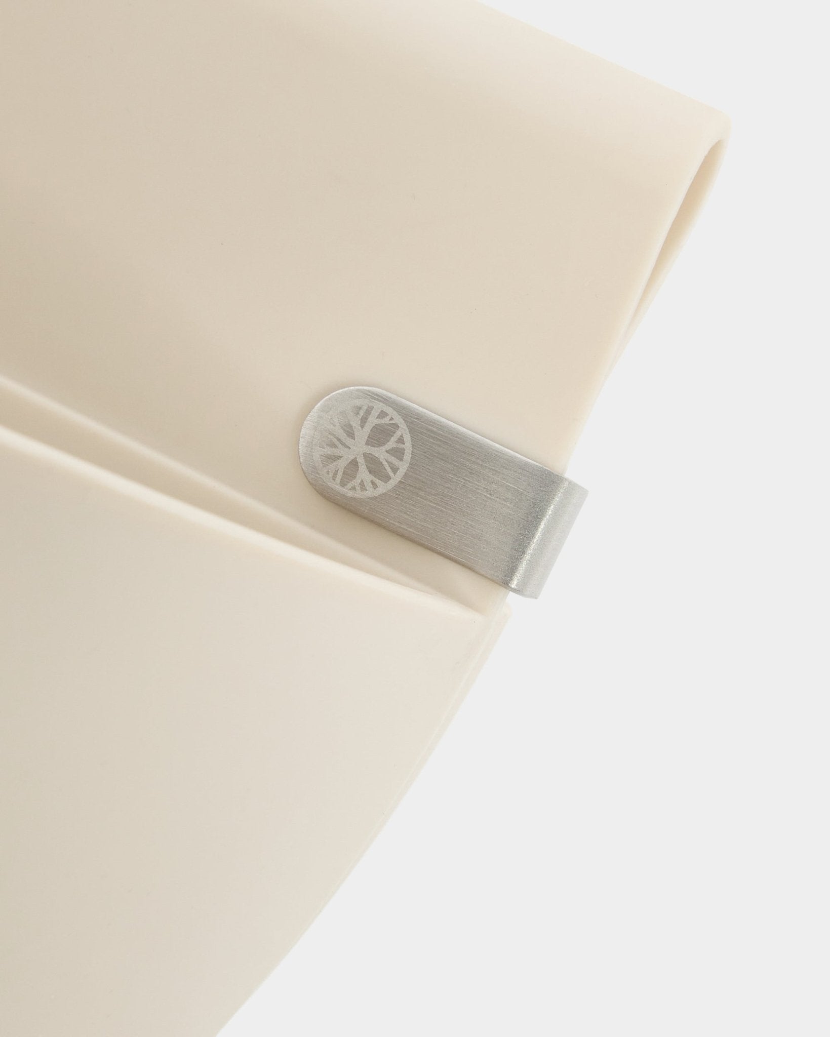 Nærbillede af et lyst beige WoodUpp Gro | Soft Pocket / BM2-panel (4 l) med metalklemme og indgraveret cirkeldetalje på en enkel hvid baggrund.