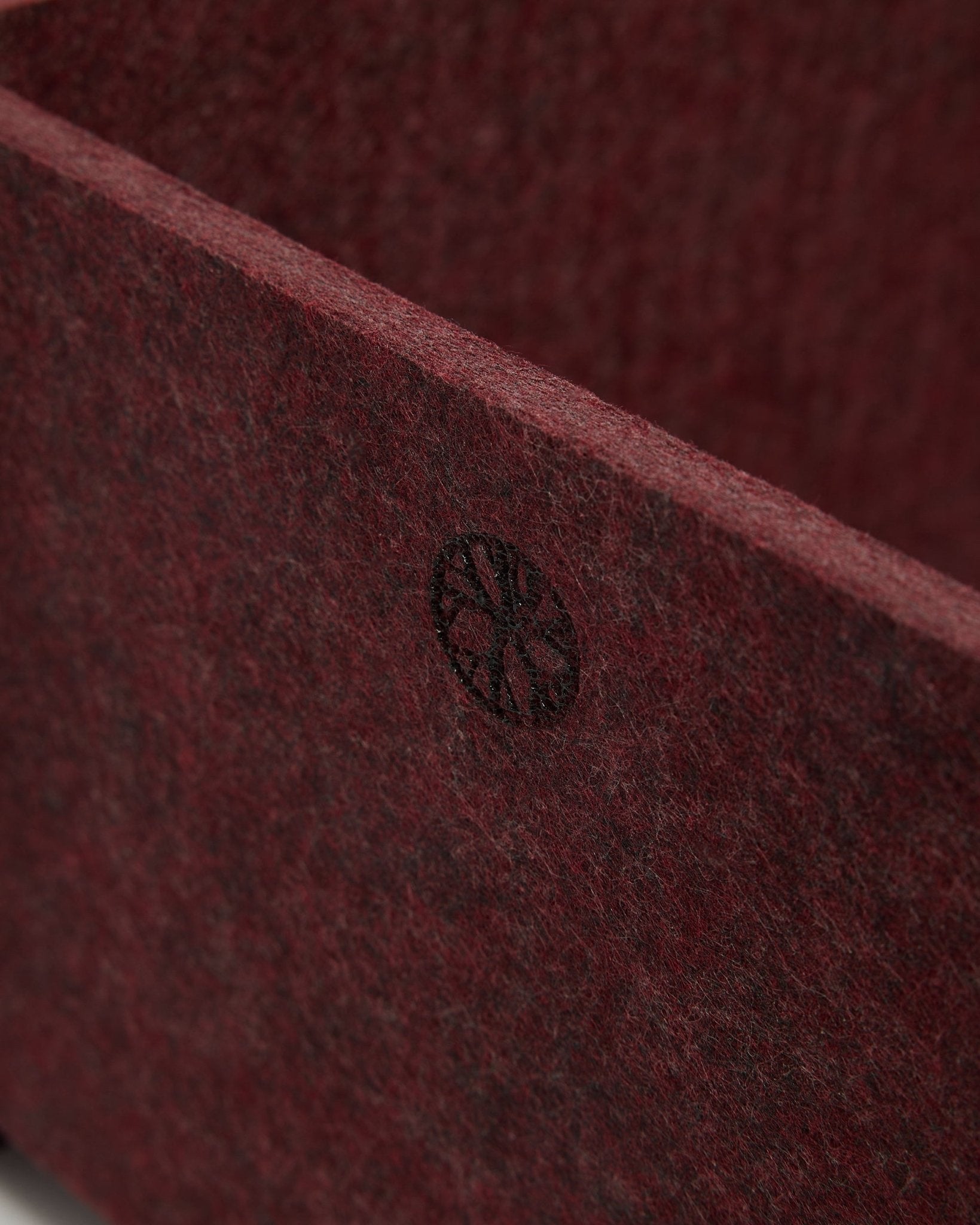 Nærbillede af WoodUpp Vigg | Felt Box / BM2 i ox red, som viser tekstureret PET-filt og et cirkulært black-emblem i hjørnet. Nordisk design af akustisk tilbehør.