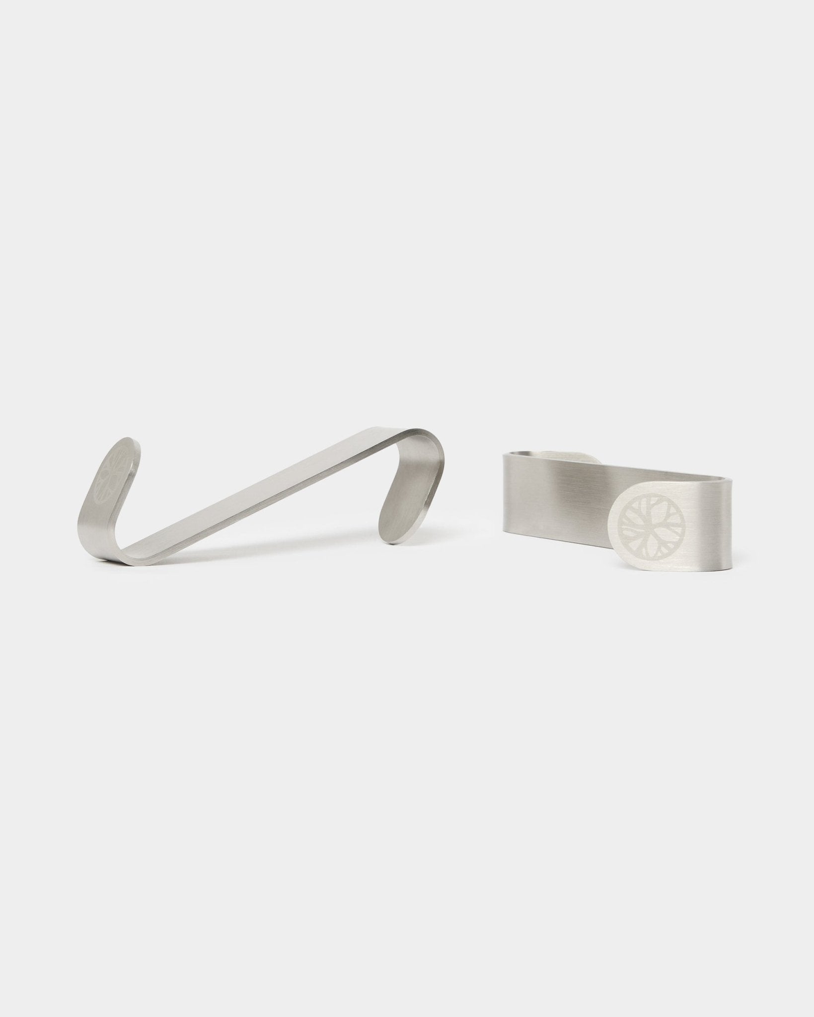 WoodUpp Alva S-krog BM1 og BM2 pengeclips, to accessories i rustfrit steel med indgraveret hjuldesign, designet til nordiske akustikpaneler i træ.