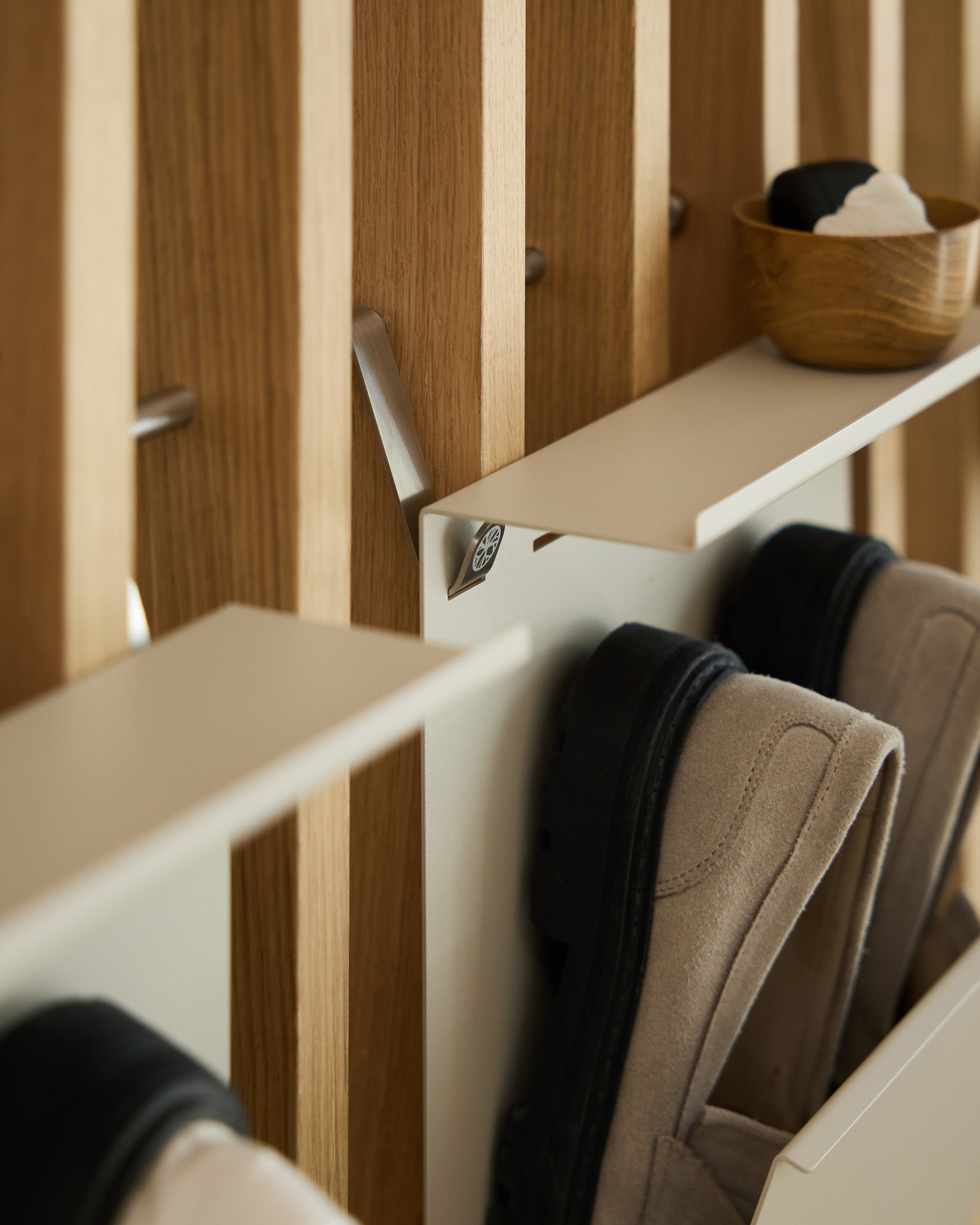 Minimalistisk skohylde i beige pulverlakeret stål fra WoodUpp monteret på et nordisk akustikpanel med lameller og en lille skål til nøgler placeret ovenpå.