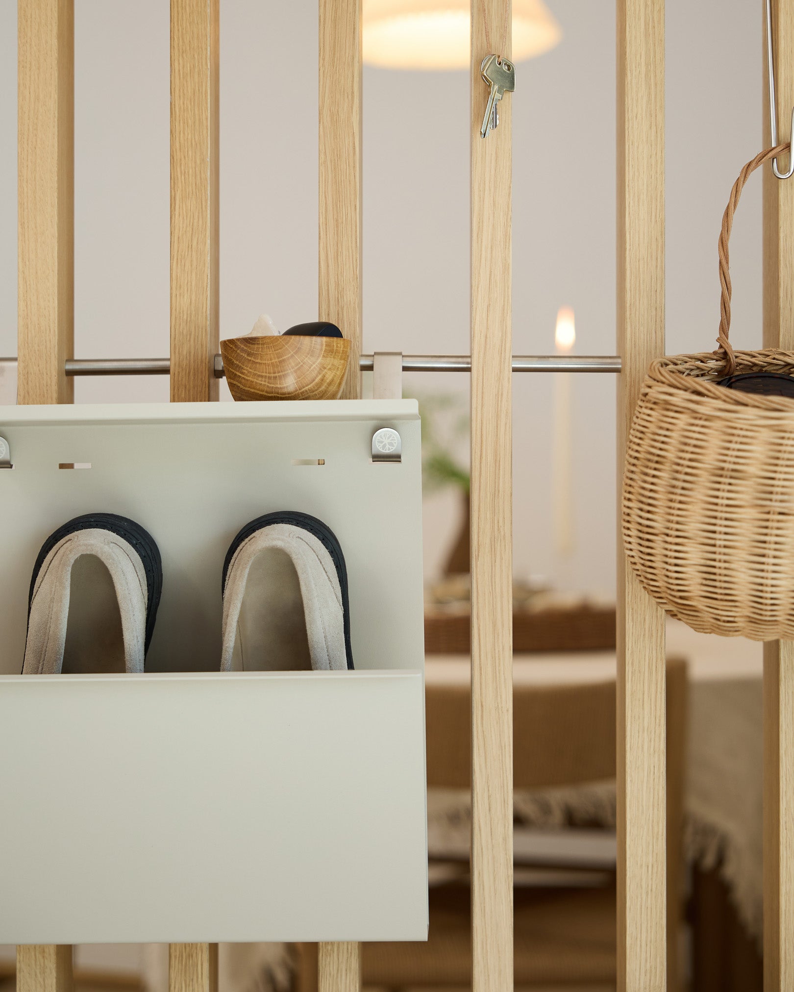 WoodUpp Nell Beige Shoe Storage viser tøfler, en skål og en flettet kurv på en rumdeler af træ; spisepladsen ses i baggrunden.