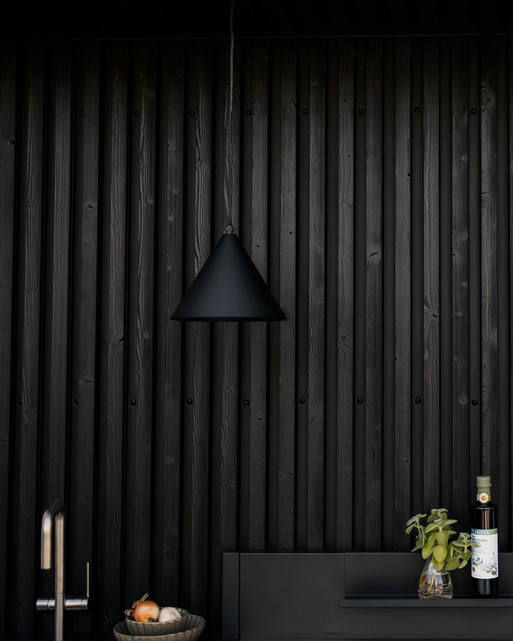 Moderne køkken med mat black pendellampe, tekstureret black Akupanel akustisk trævæg og bordplade med grøntsager, frisk basilikum og olivenolie.