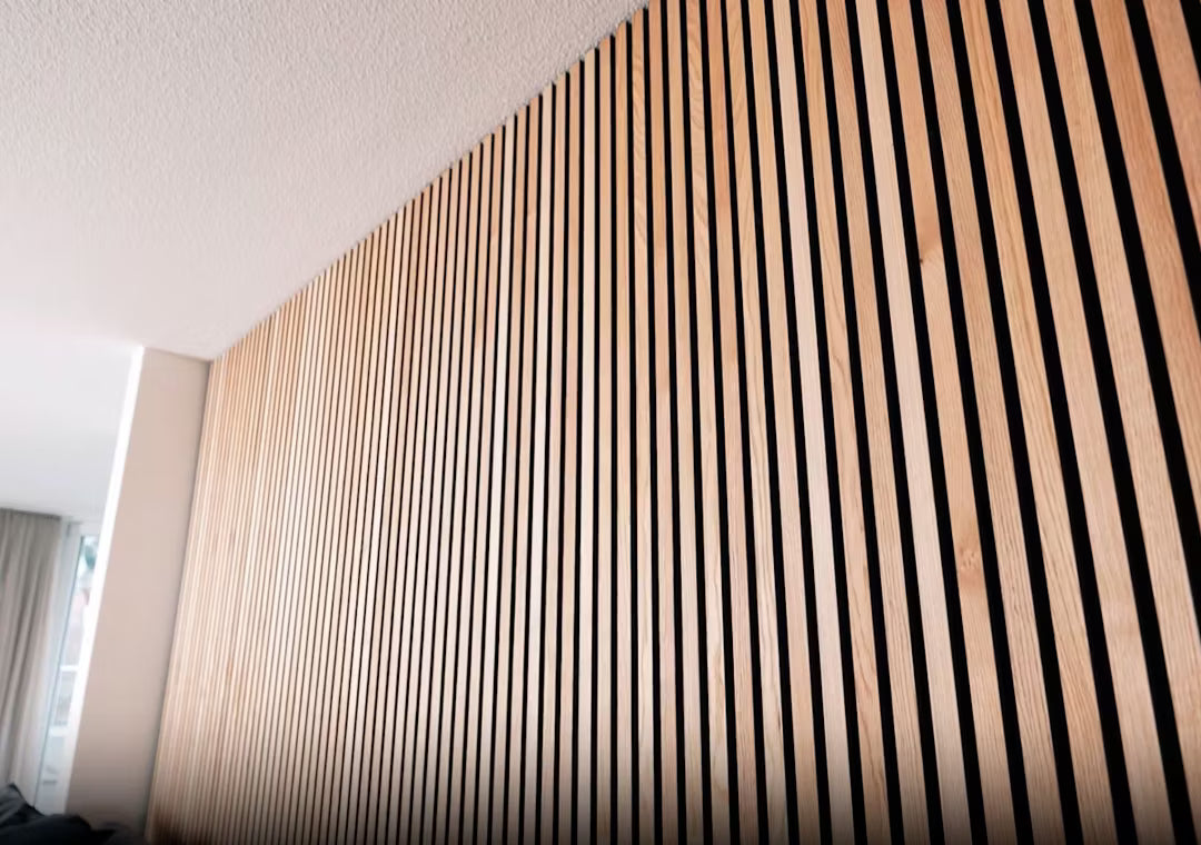 Nærbillede af Akupanel akustisk træpanel med lodrette trælameller i et stribet mønster, installeret på en indvendig væg under et hvidt loft.