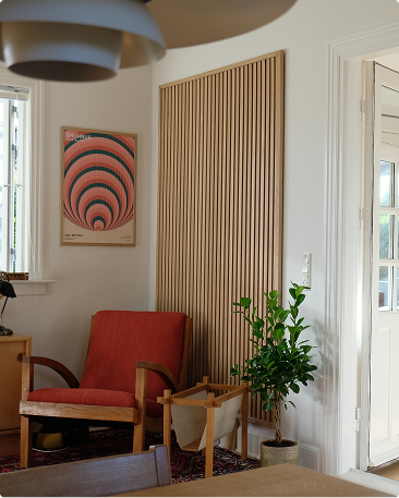 Corner with a red armchair, potted plant, acoustic wood slat paneling on the wall, and natural light from a window and open door in a bright room.