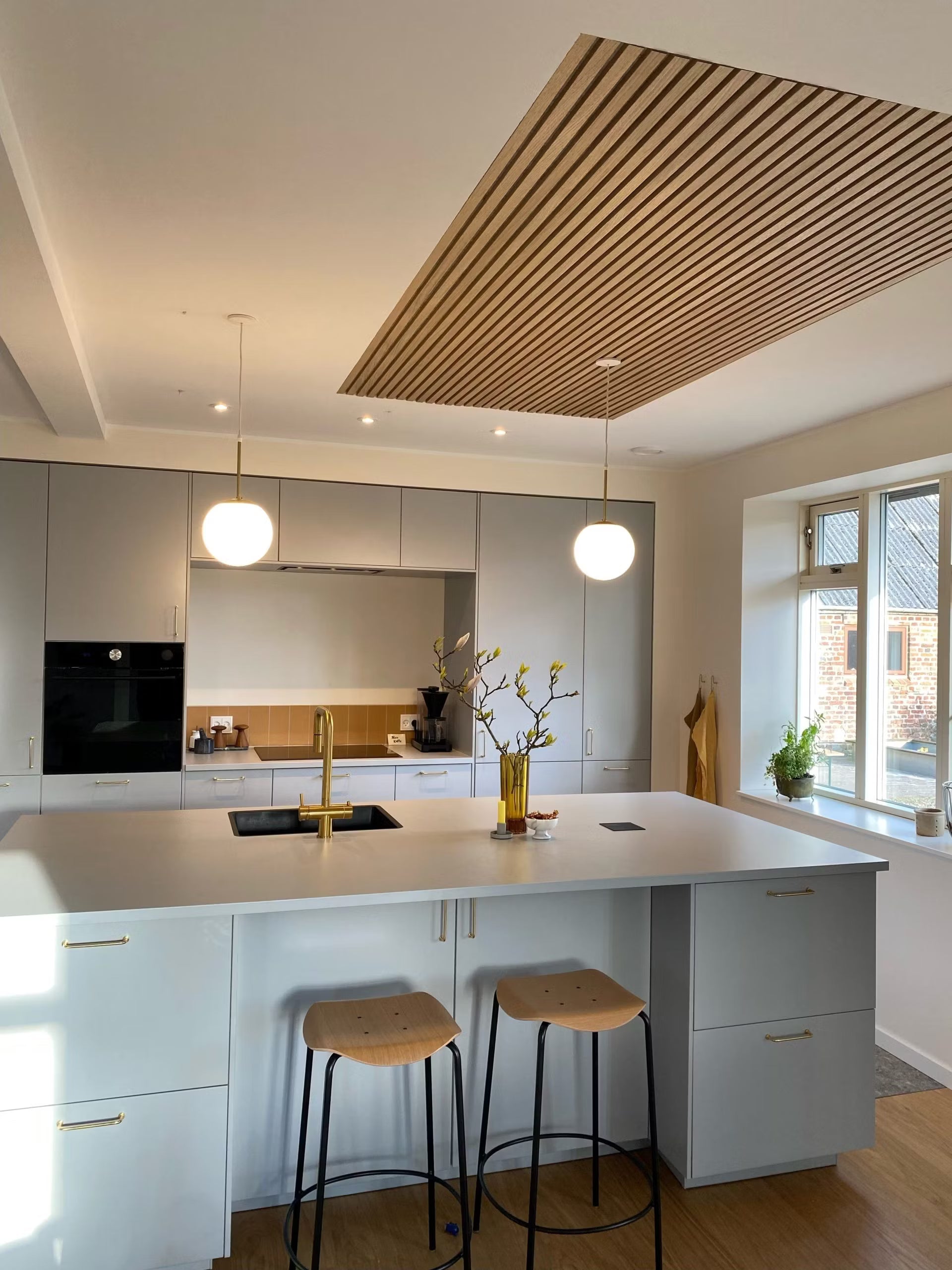 Akupanel wood slat ceiling panel inset in white ceiling above kitchen island.