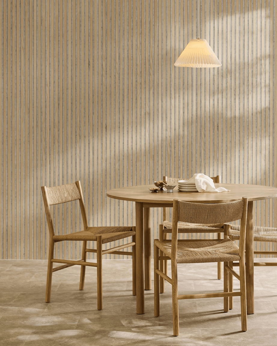 Minimalistisk spiseområde med et rundt træbord, flettede stole, en pendellampe og et WoodUpp Akupanel akustikpanel i træ i Classic Oak med grey filt.