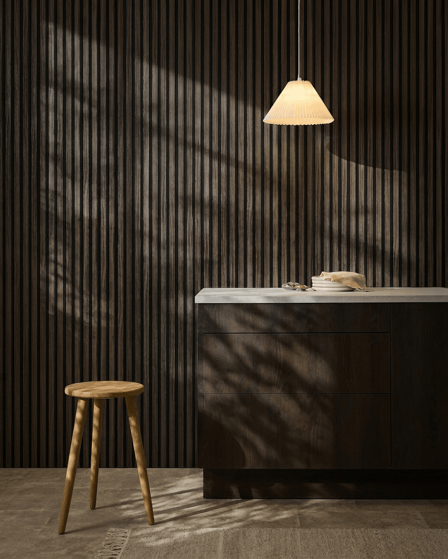 Minimalistisk køkken med WoodUpp Akupanel Black Oak akustikpaneler på væggen, træskammel, hvid bordplade, beige pendellampe og soloplyste skygger.