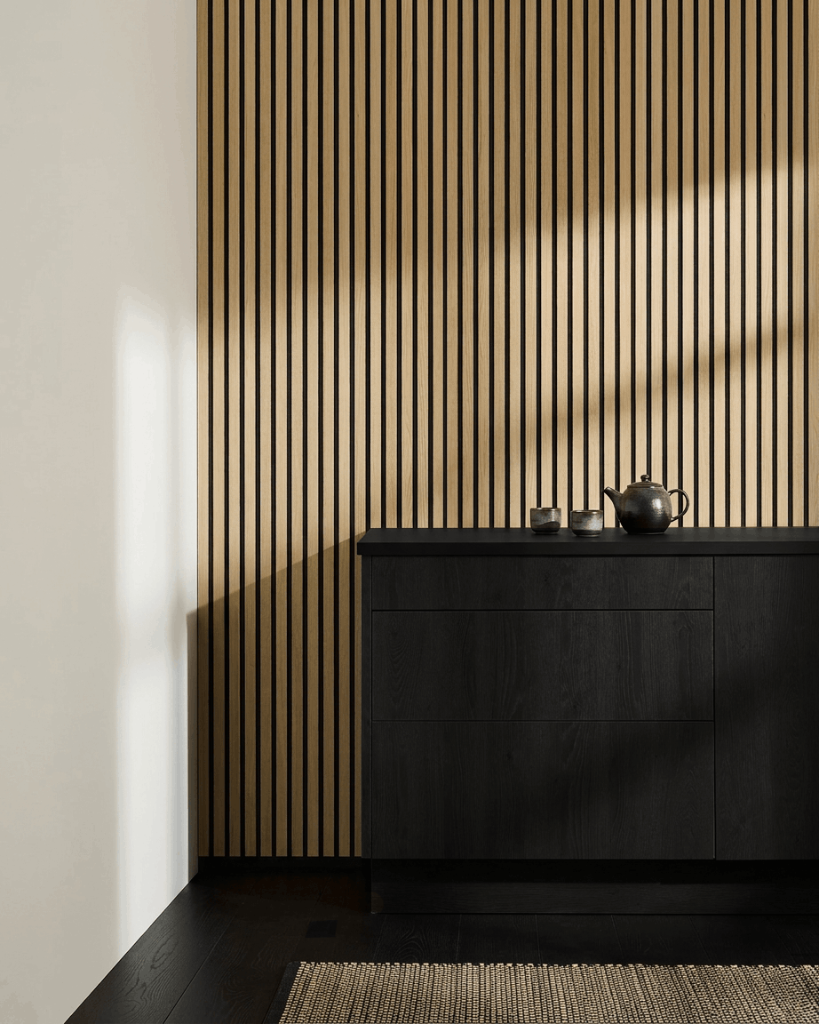 Minimalistisk nordisk køkken med WoodUpp Akupanel Akustikpanel i Classic Oak, black skab, tekande, kopper og vævet tæppe på mørkt trægulv.