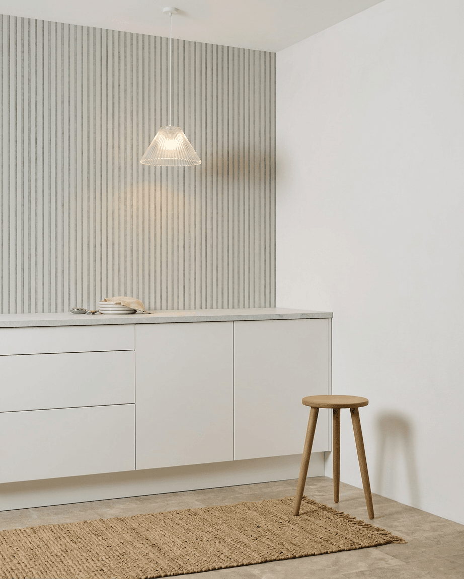 Minimalistisk køkken med hvide skabe, en træskammel, et vævet tæppe og et WoodUpp Akupanel Snow Akustikpanel installeret for lydabsorption.