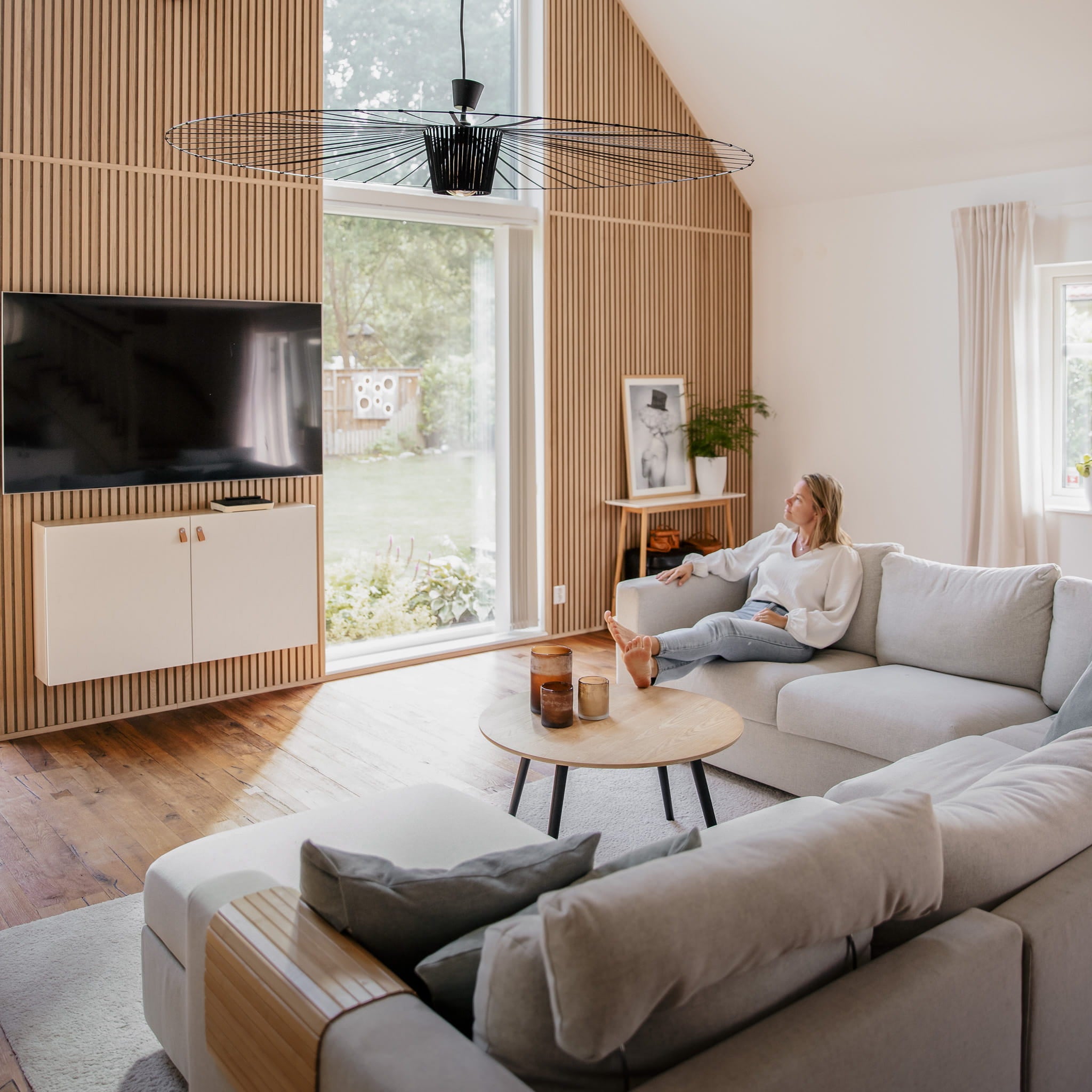 Woman sitting on a couch in a modern living room with large windows facing Akupanel in classic oak.